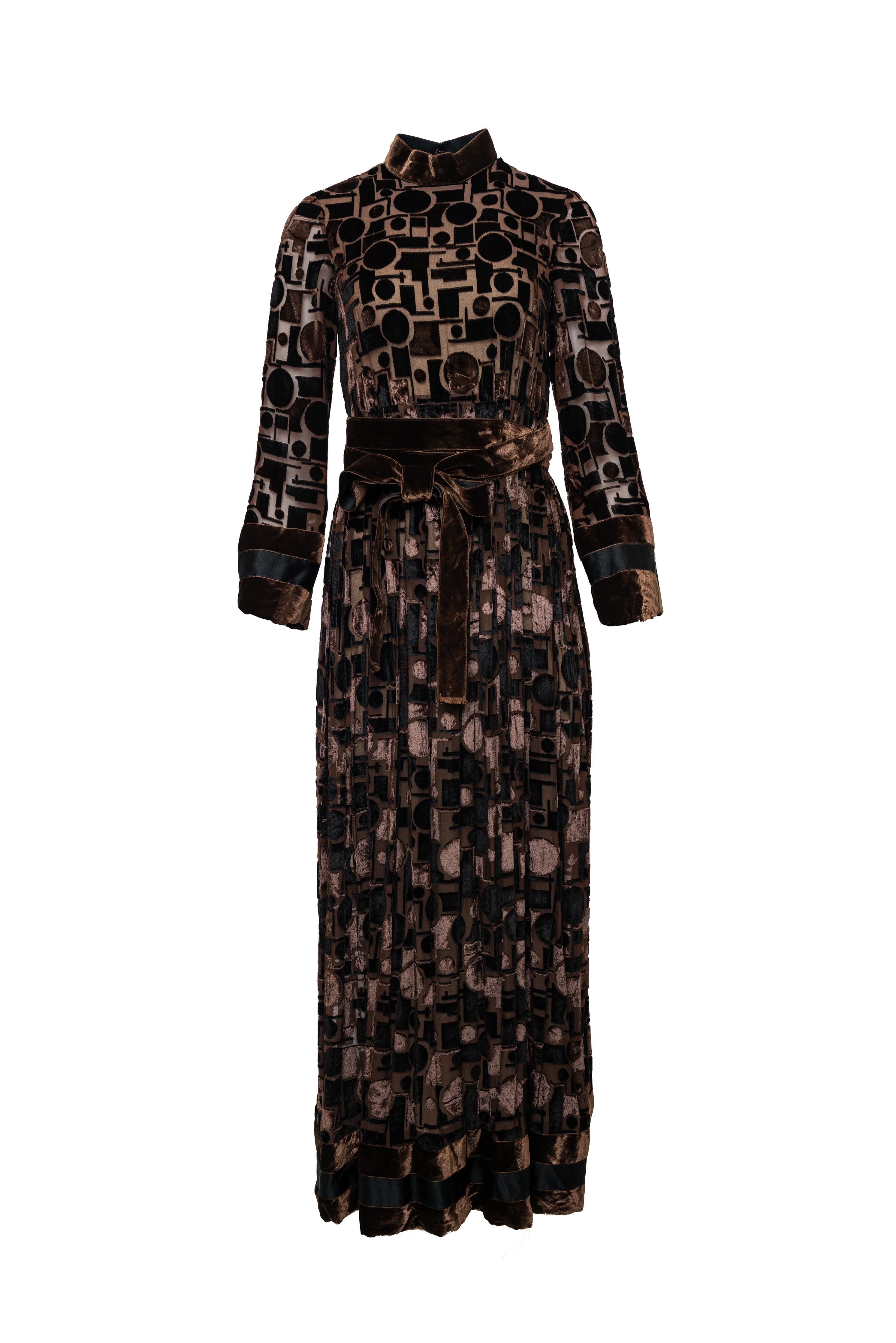 Dieses Meisterwerk von Geoffrey Beene präsentiert sich mit luxuriösem, gebranntem Samt in sattem Schokoladenbraun - eine raffinierte Wahl für Ihre unvergesslichen Winterabende. Die langen Ärmel und die eingeschnürte Taille sorgen für eine elegante