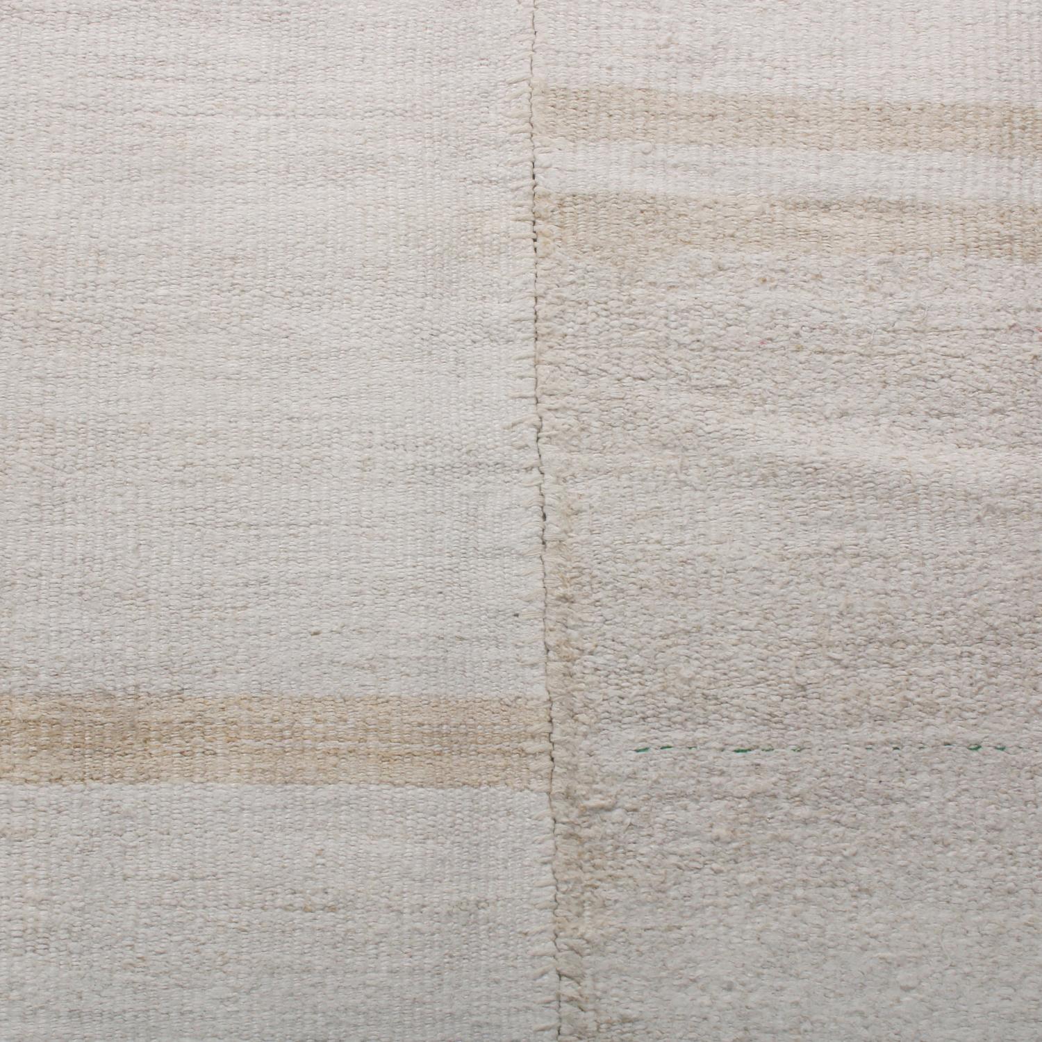 Dieser handgewebte, aus der Türkei stammende Kelim-Teppich aus Wolle, der zwischen 1970 und 1980 hergestellt wurde, zeichnet sich durch ein Spiel aus subtilen Beige- und Off-White-Farbvariationen aus, die die schlichte, beruhigende Geometrie mit