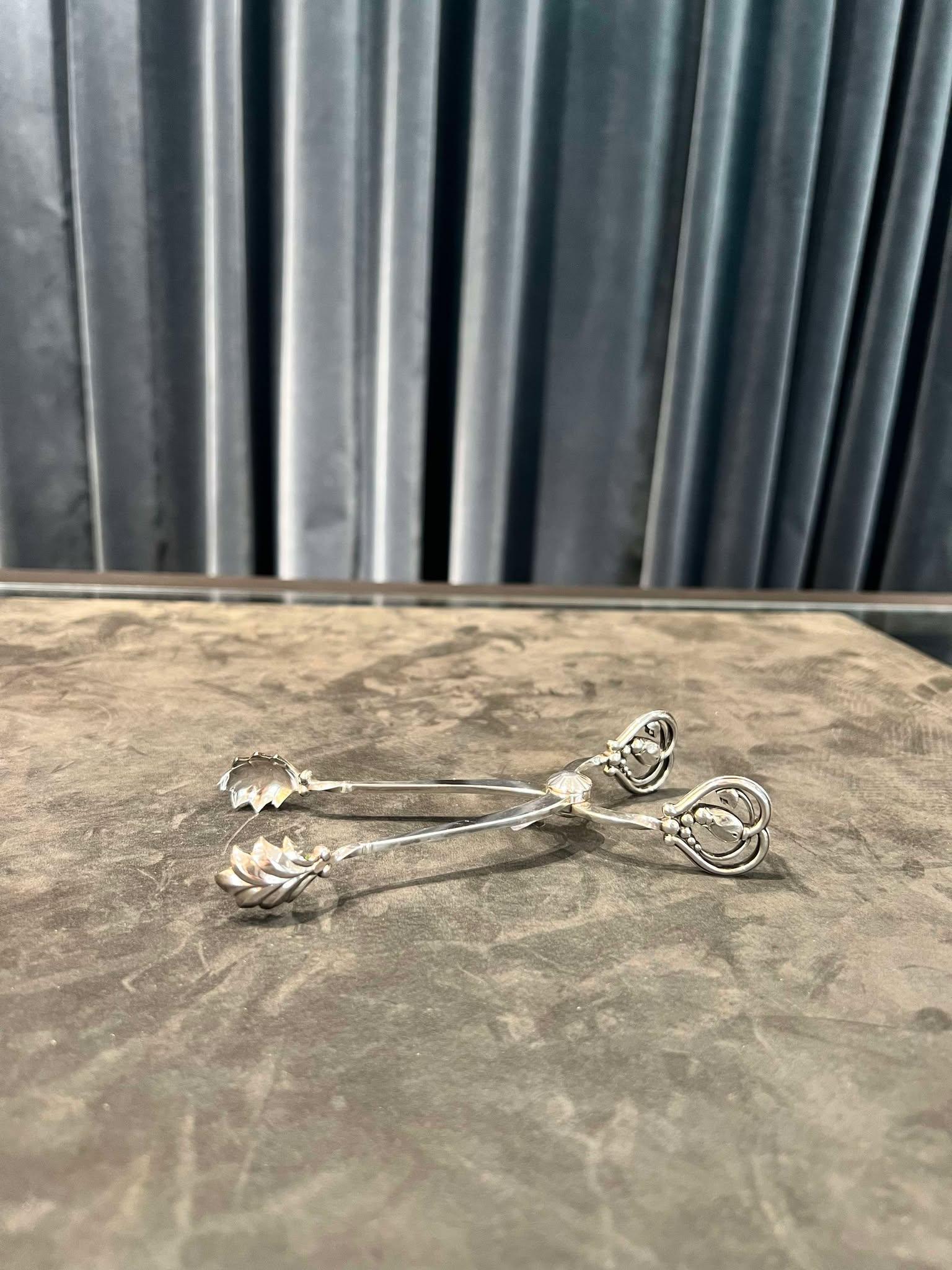 Un par de pinzas para hielo de plata de ley de Georg Jensen, con el diseño Ornamental nº 132. Las asas están bellamente elaboradas con un motivo de flores, unidas a un par de tijeras de esterlina con extremos en forma de garra para recuperar los