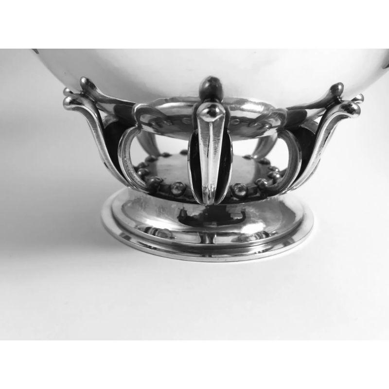 This is a sterling silver Georg Jensen footed bowl, design #584B by Oscar Gundlach-Pedersen from circa 1929.

This hand-hammered bowl stands on a raised foot decorated with silver balls and a pedestal of stylistic leaves.

Additional