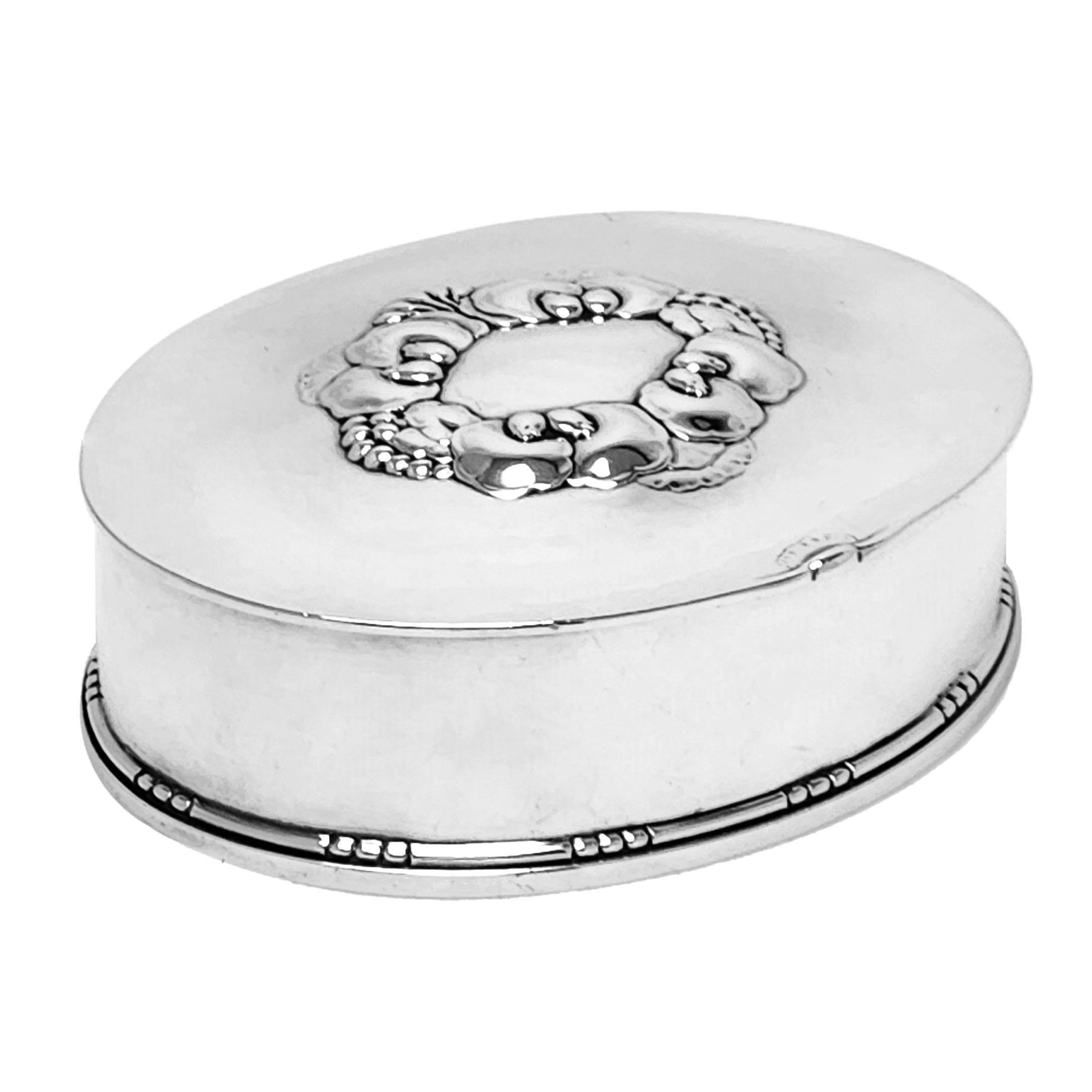 A beautiful vintage Georg Jensen silver box with an oval shape. The Lid of the Box has a stylised floral cartouche and features a subtly hammered finish. The base of the box is decorated with an understated bead border. 

The Box is Georg Jensen