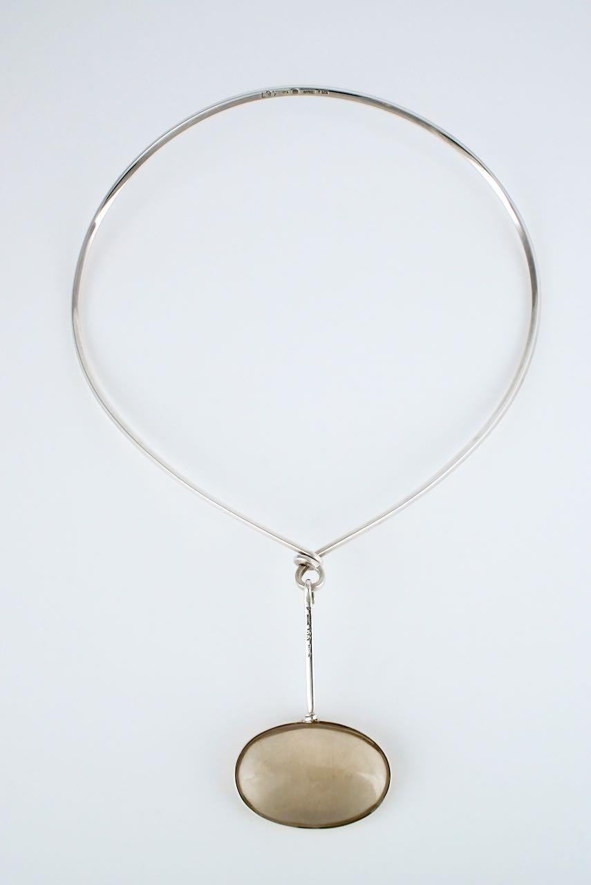A vintage solid silver and oval rutilated quartz pendant neck ring featuring a beautiful oval double sided cabochon of rutilated smoky quartz wrapped with wire and suspended crossways from a hooked graduated rod and hanging from a loop on a