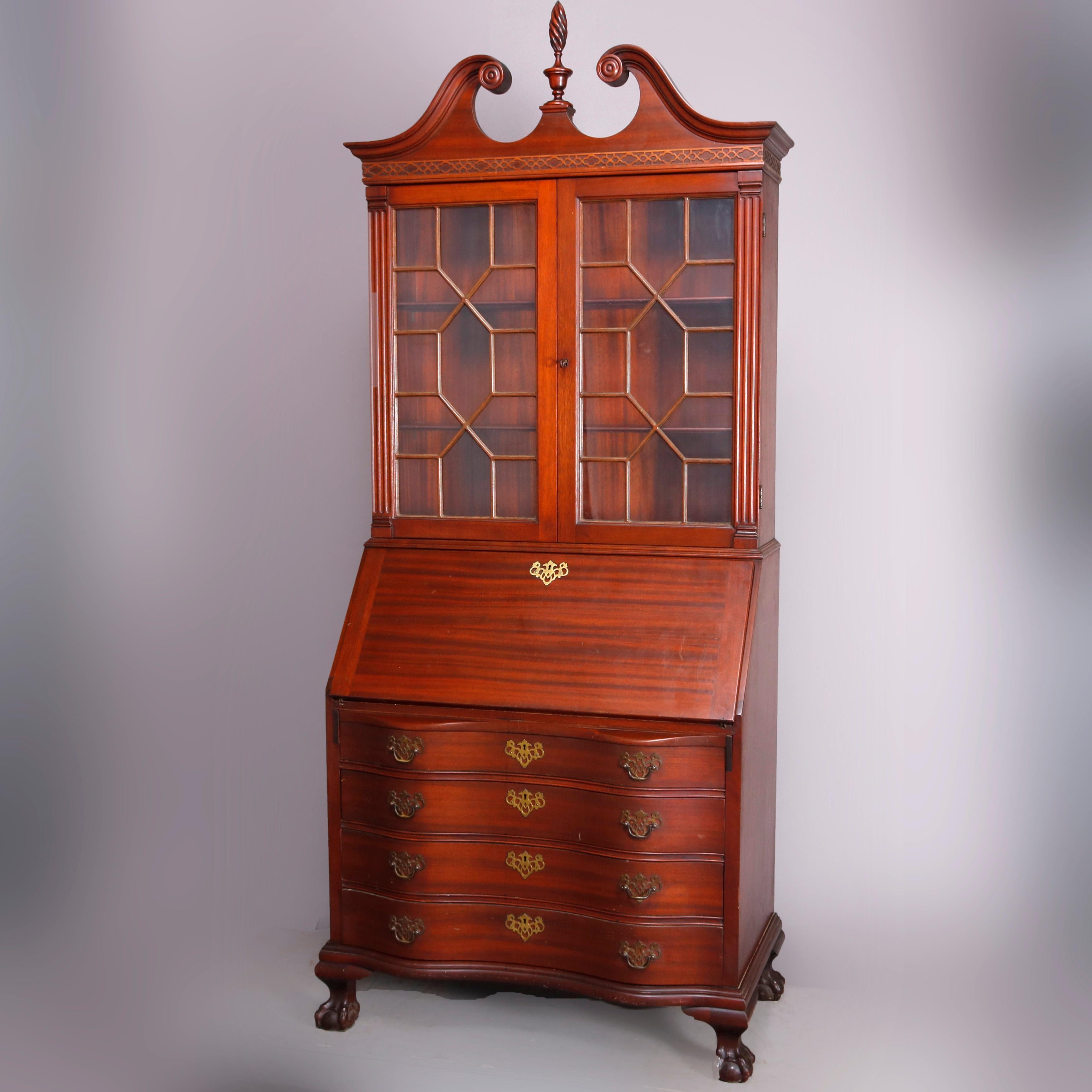 A vintage George Winthrop secretary features mahogany construction with upper case having broken arch crest with stylized flame finial surmounting bookcase with double mullioned glass doors opening to shelved interior, lower serpentine case having