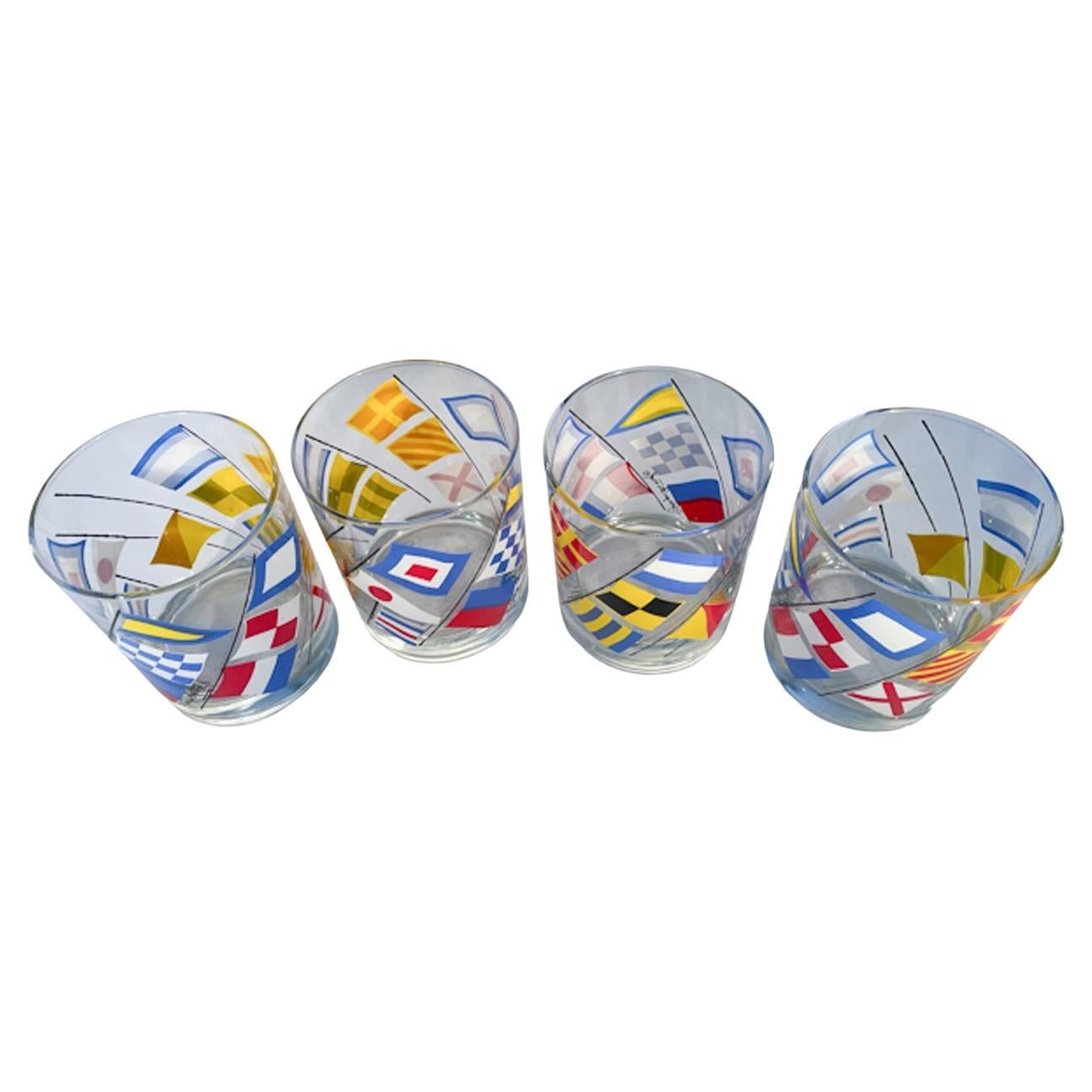 Four large rocks glasses designed and signed by Georges Briard in clear glass decorated with nautical signal flags in brightly colored enamels.