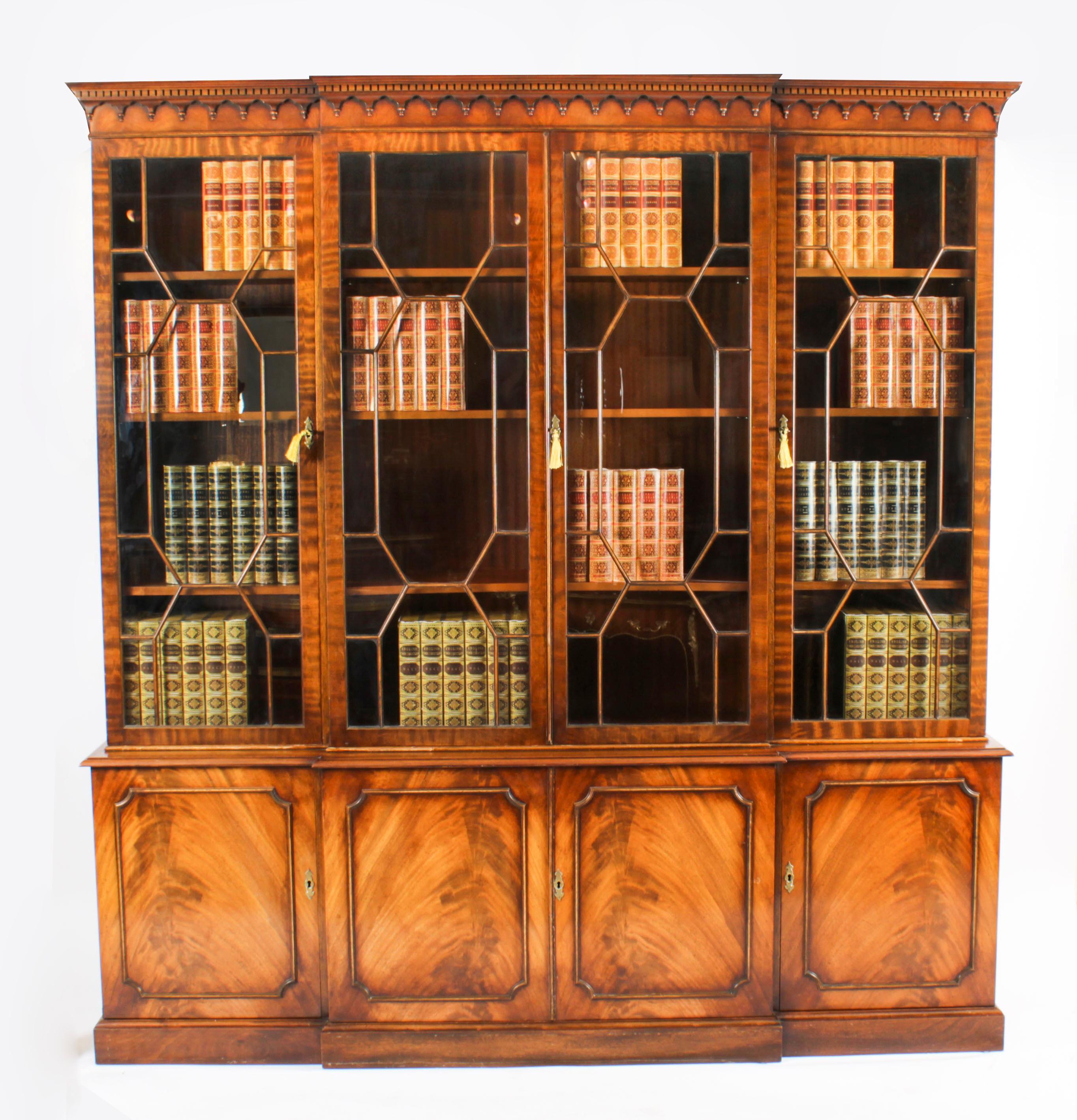 A delightful Vintage flame mahogany Georgian Revival library breakfront bookcase, dating from the mid 20th Century.

The top features a moulded cornice with a dental and arcaded frieze. The four astragal glazed doors open to reveal three