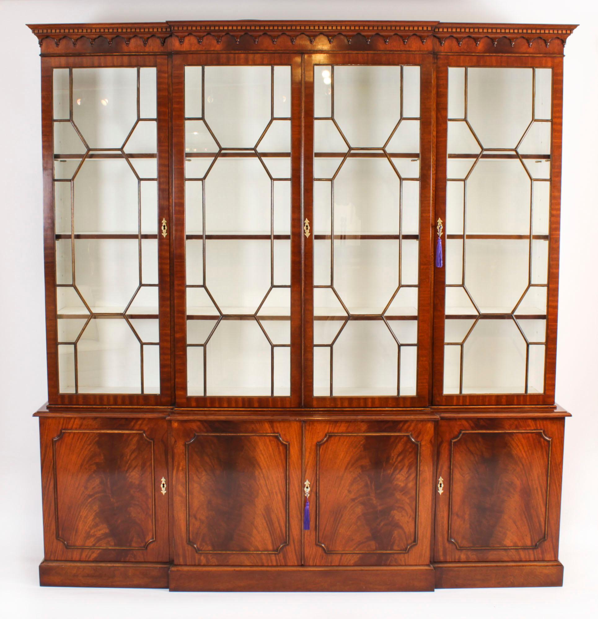A delightful Vintage flame mahogany Georgian Revival library breakfront bookcase, dating from the mid 20th Century.

The top features a moulded cornice with a dental and arcaded frieze. The four astragal glazed doors open to reveal three adjustable