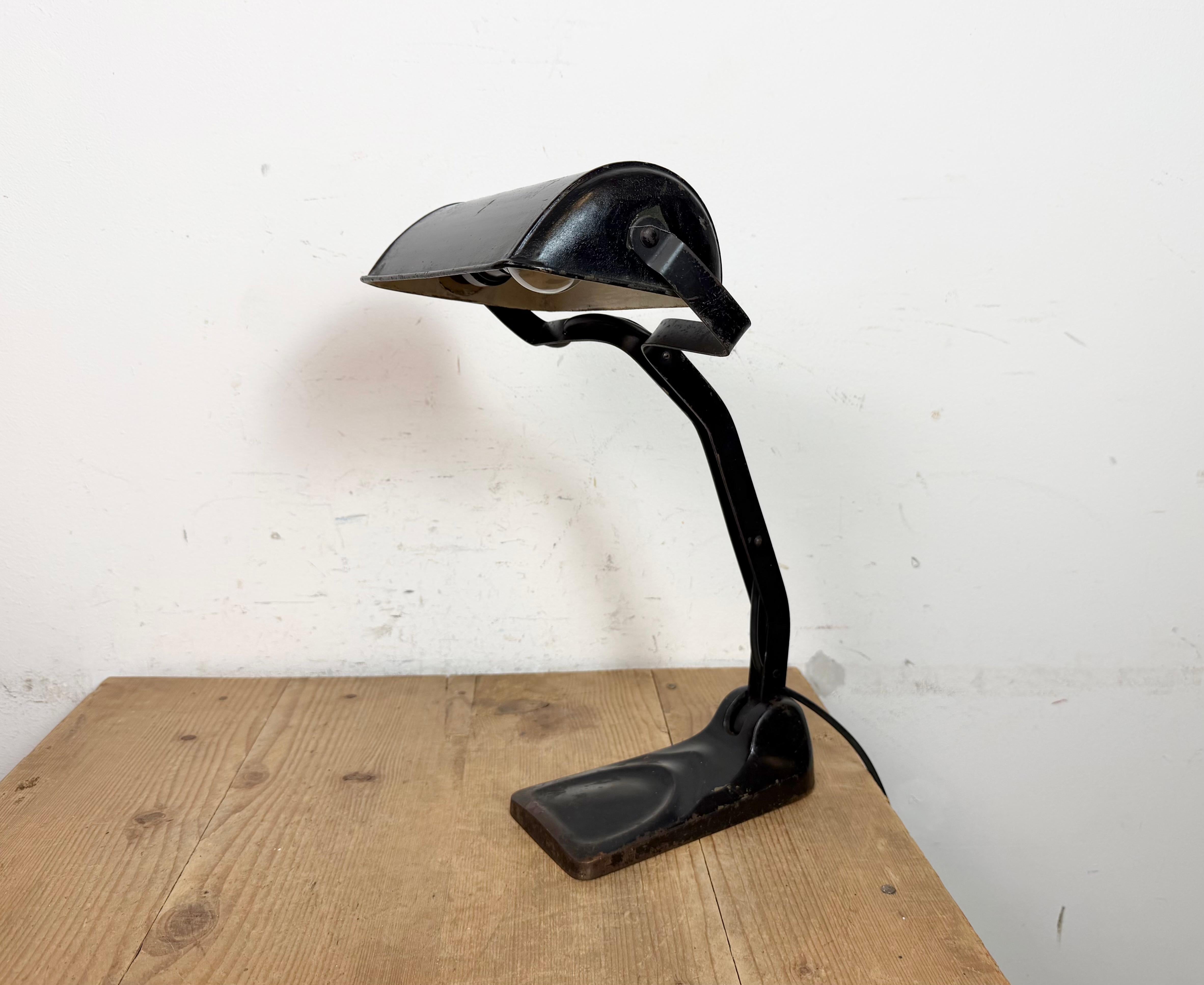 Lámpara de mesa vintage bankers bauhaus fabricada en Alemania en la década de 1930. Presenta una pantalla de hierro metálico negro con el interior blanco y una base de hierro fundido negro. El brazo y la pantalla son regulables. El enchufe  requiere