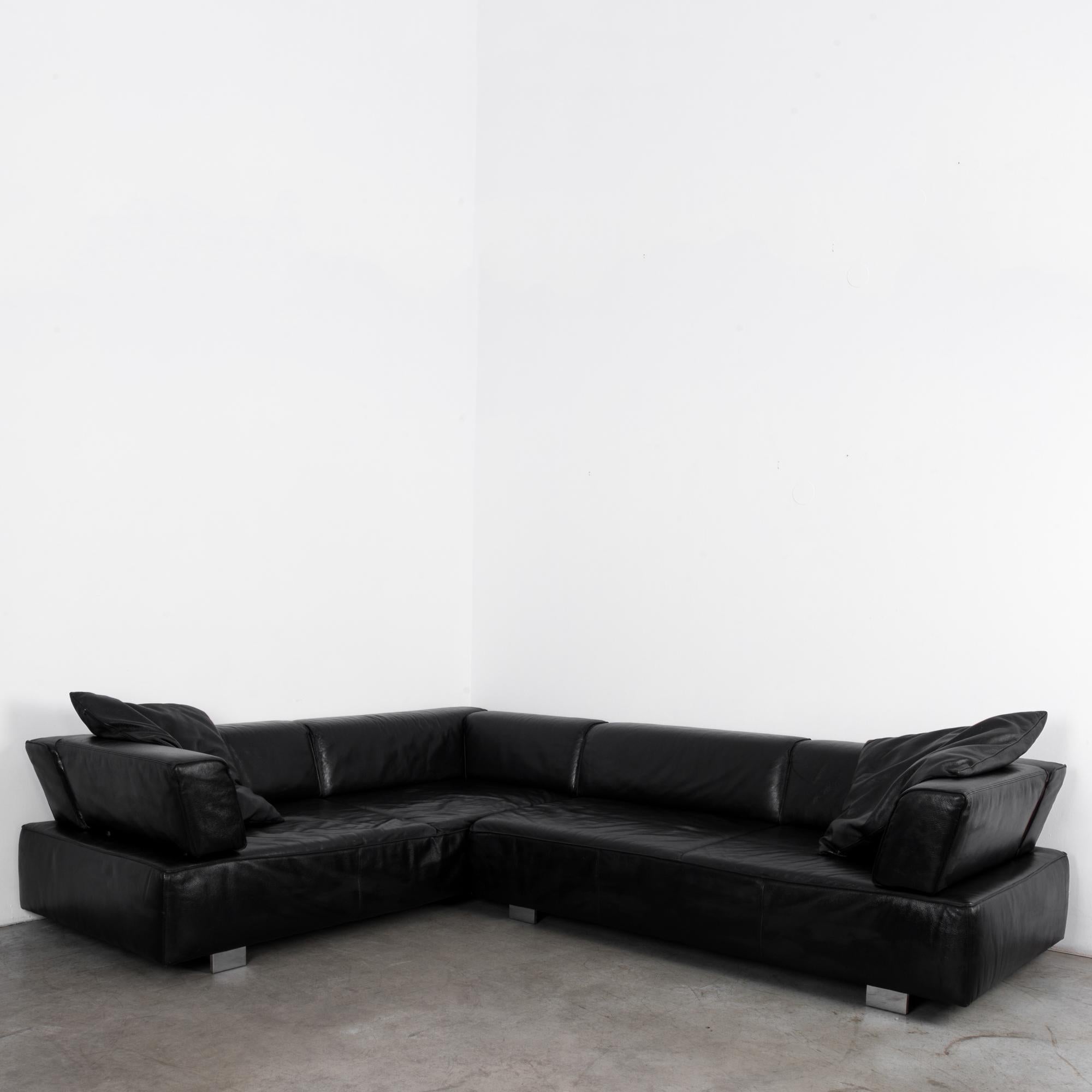 A black leather corner sofa from Germany, by furniture designers Brühl & Sippold. The bed of the sofa is ample, raised upon silver feet. The backrests, which sit at a reclined slant, lend the box-like shape a stylish angularity. The leather is a