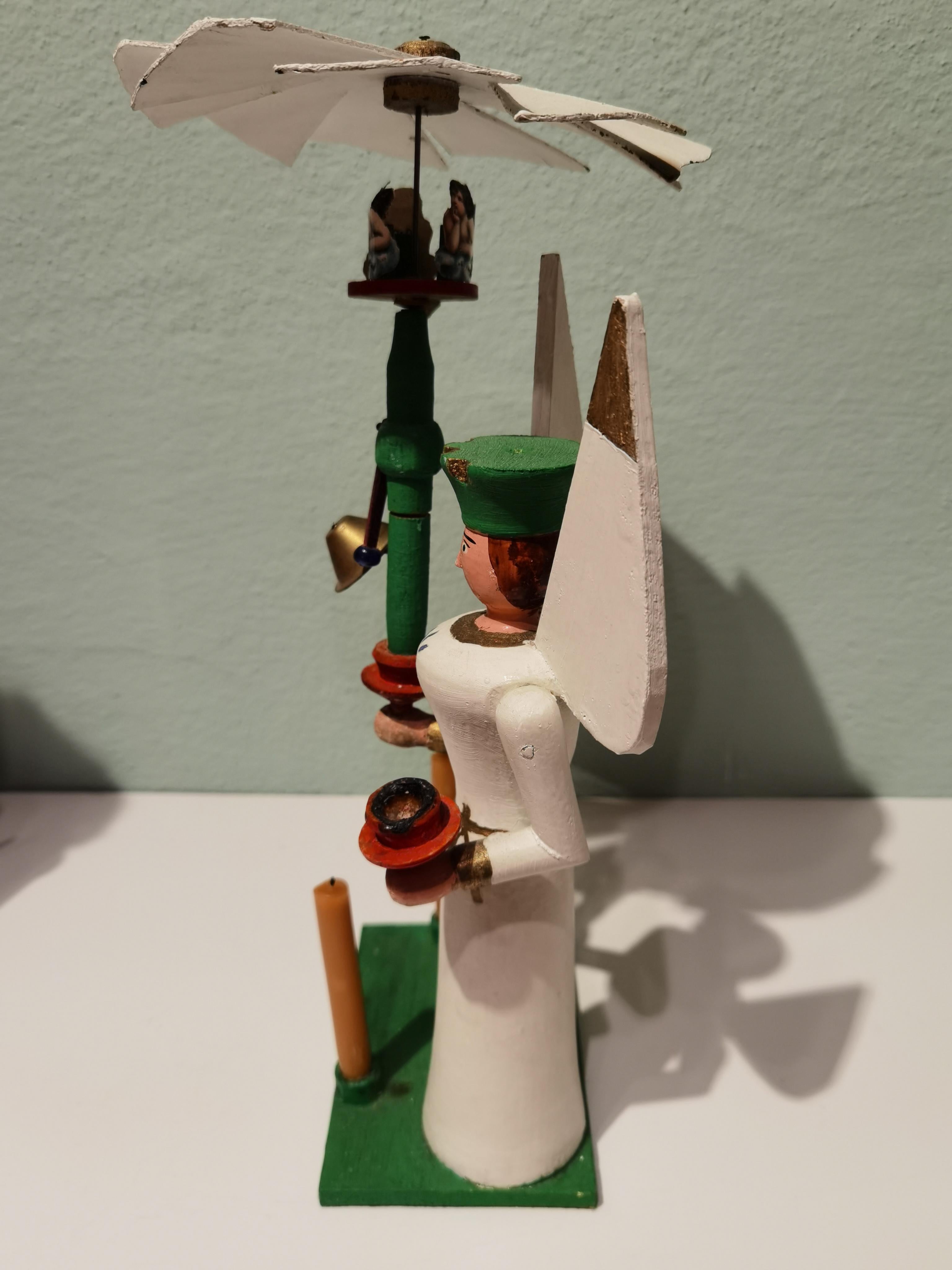 Vintage German Christmas angel sculpture handmade in wood. From the Erzgebirge. The traditional hand carved angel is hand painted and stands on a rectangular green wooden plateau.
The heat of the 3 burning candles activates the play. The sculpture