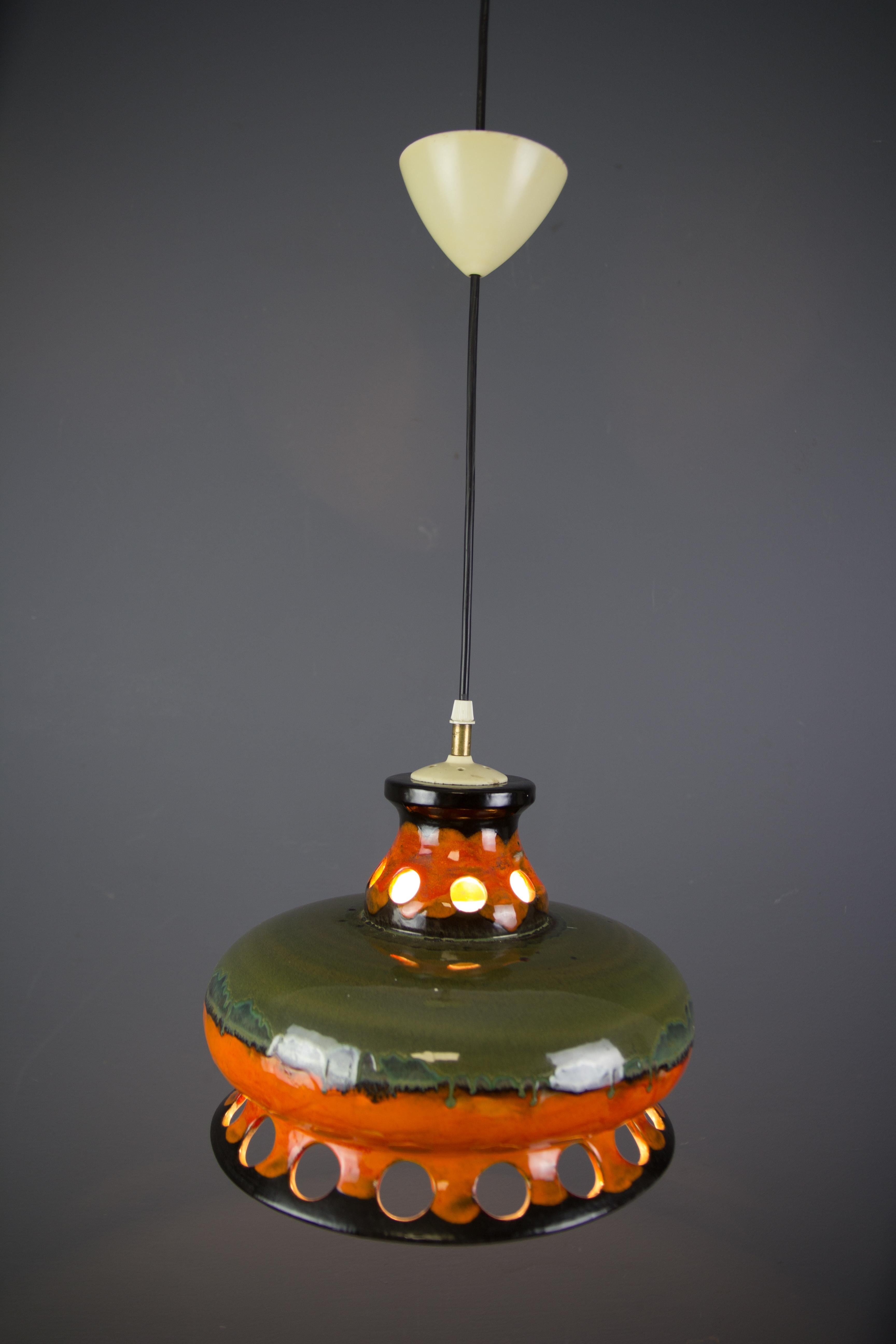 Colorful orange, green, and black German Ceramic Fat Lava or West German Pottery pendant ceiling light, glazed outside and inside. The light comes through the circles creating wonderful shadows on the wall. Adjustable height and one socket for the