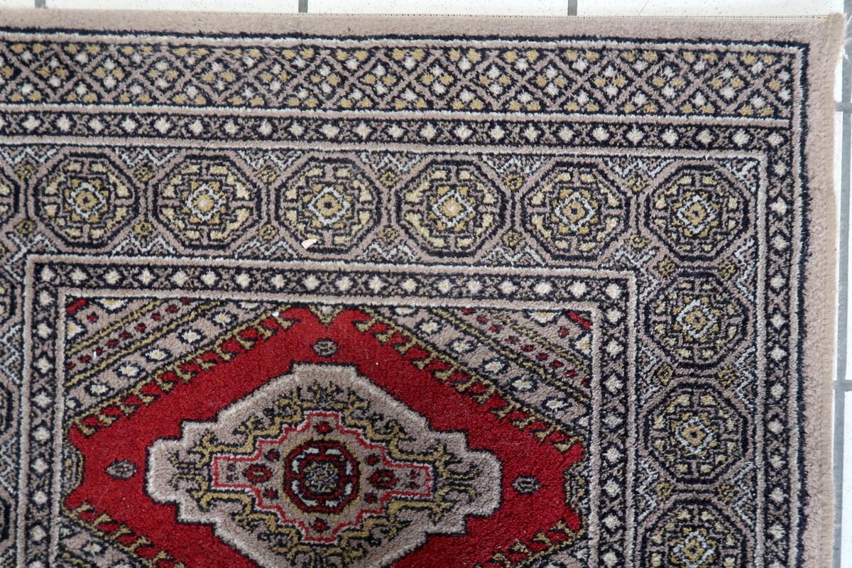 This vintage German geometric rug from the 1970s is a stylish and durable machine-made piece, featuring a striking traditional geometric pattern. The rug's rich red base is adorned with intricate beige, black, and gold motifs, creating an elegant