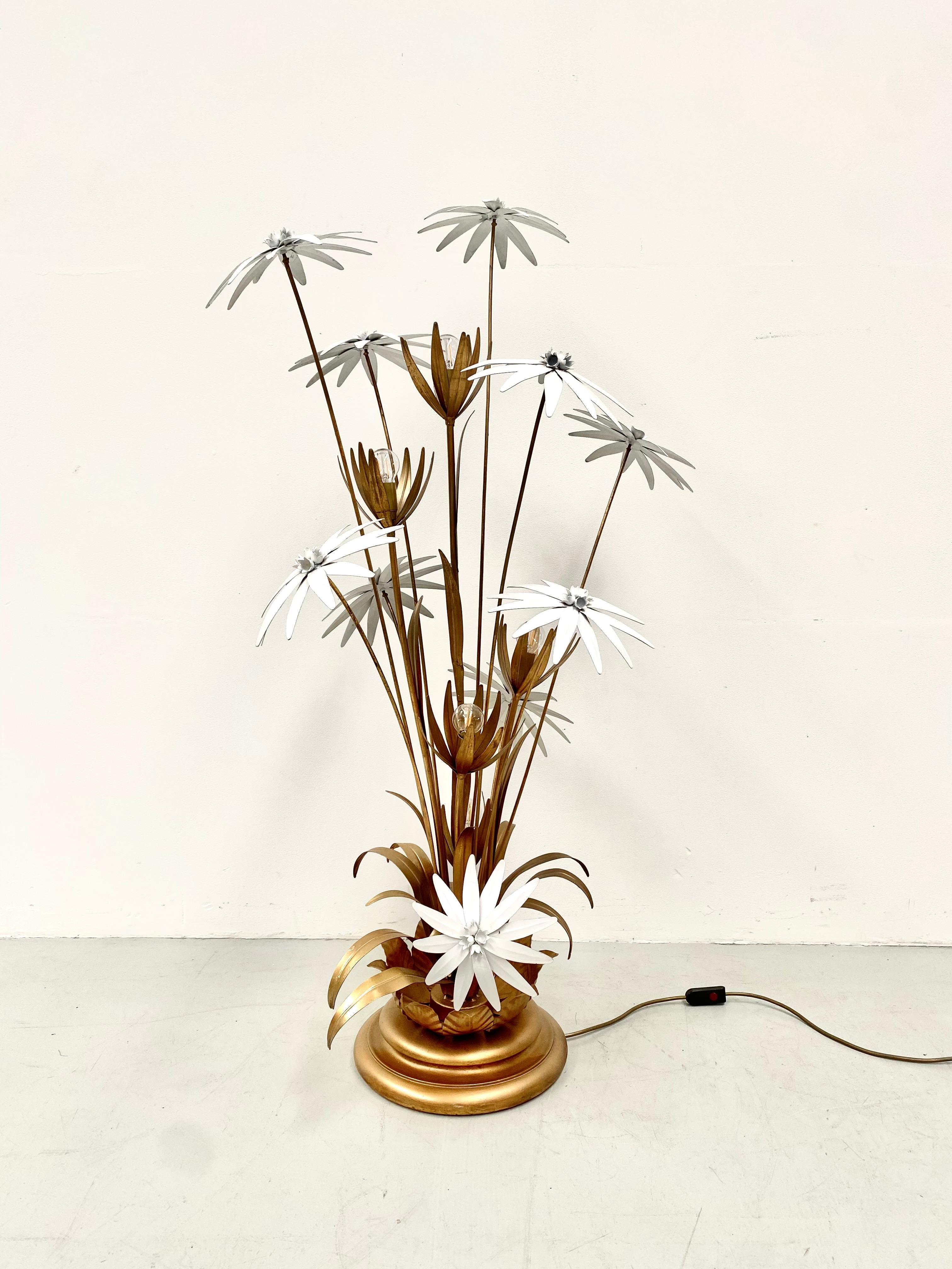 The floorlamp features a solid gilded round base with gilt metal flower stalks with leaves and on top white enamelled flowers. This floorlamp in Hollywood regency style was designed by the German Hans Kögl in the seventies.The position of the light