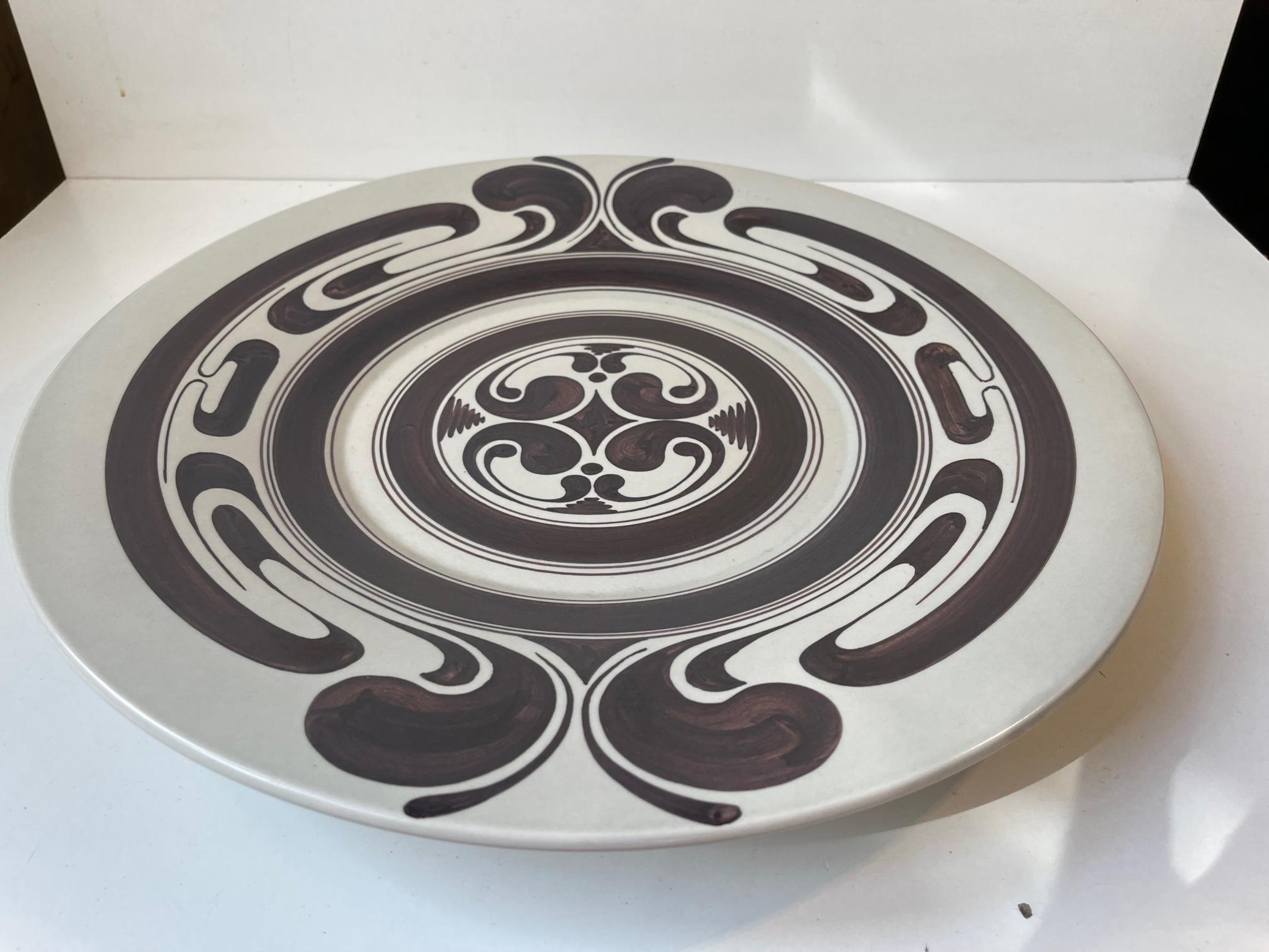 Large decorative charger dish, centerpiece or wall plaque in handpainted ceramics. Designed and made at Rosenthal in Germany circa 1970-80. It features a skillfully and 'quick' executed center motif in a dark brown/burgundy color. Very fine vintage