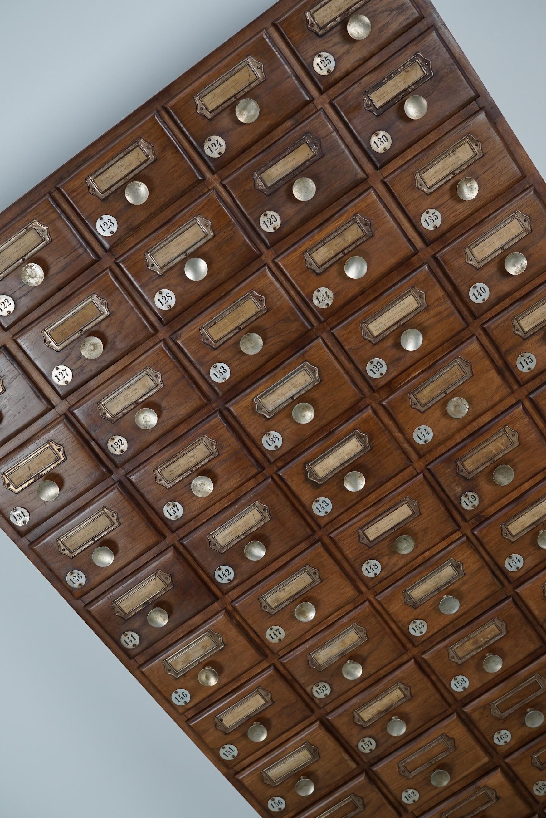 Cette armoire à pharmacie a été fabriquée vers les années 1950 en Allemagne. Il était utilisé pour stocker les économies dans un bar ou une sorte de club. Il comporte de nombreux tiroirs avec des boutons et des numéros en métal. De nombreux labels