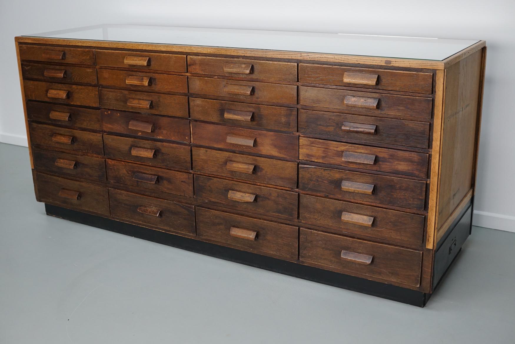 Questo bancone da merceria in rovere risale agli anni '50 ed è stato realizzato in Germania. Presenta una struttura in legno massiccio, un involucro in vetro e molti cassetti in Oak. I divisori possono essere rimossi, si inseriscono e si fissano con