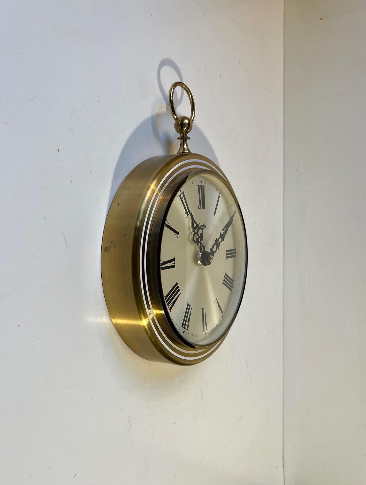 A pocket watch shaped quartz (batteri-operated) wall clock featuring solid brass frame, Roman numerals and a sunburst dial in silver enamel. Manufactured by Genfa in Germany circa 1970-80. Measurements: H: 24.5, Diameter: 18.5 cm.