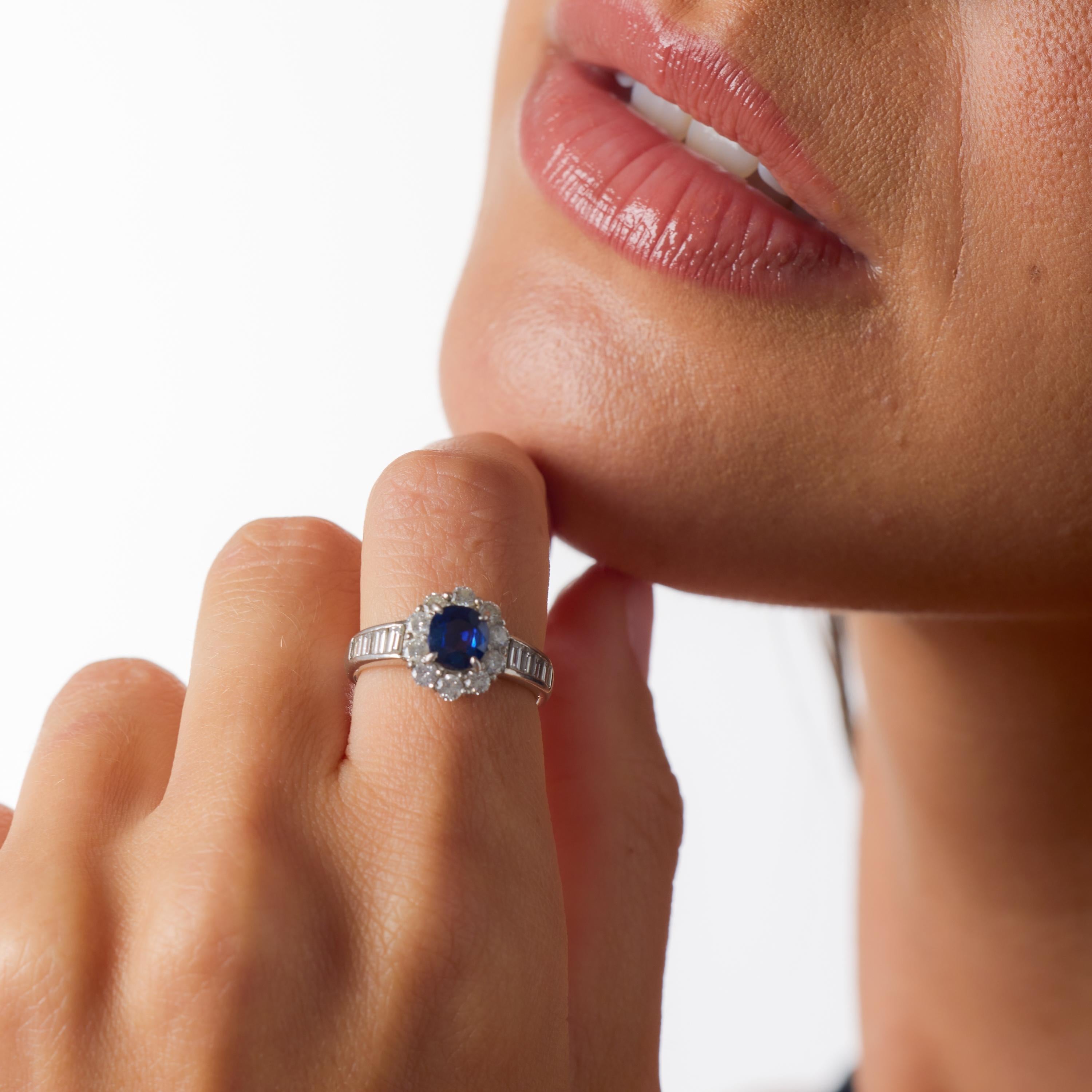 Dieser strahlende Vintage-Cluster-Ring fängt die zeitlose Eleganz der Saphir- und Diamantenkunst ein. Im Mittelpunkt steht ein GIA-zertifizierter 1,06-karätiger Saphir aus Madagaskar. Seine ovale Silhouette leuchtet in einem satten Blauton, der