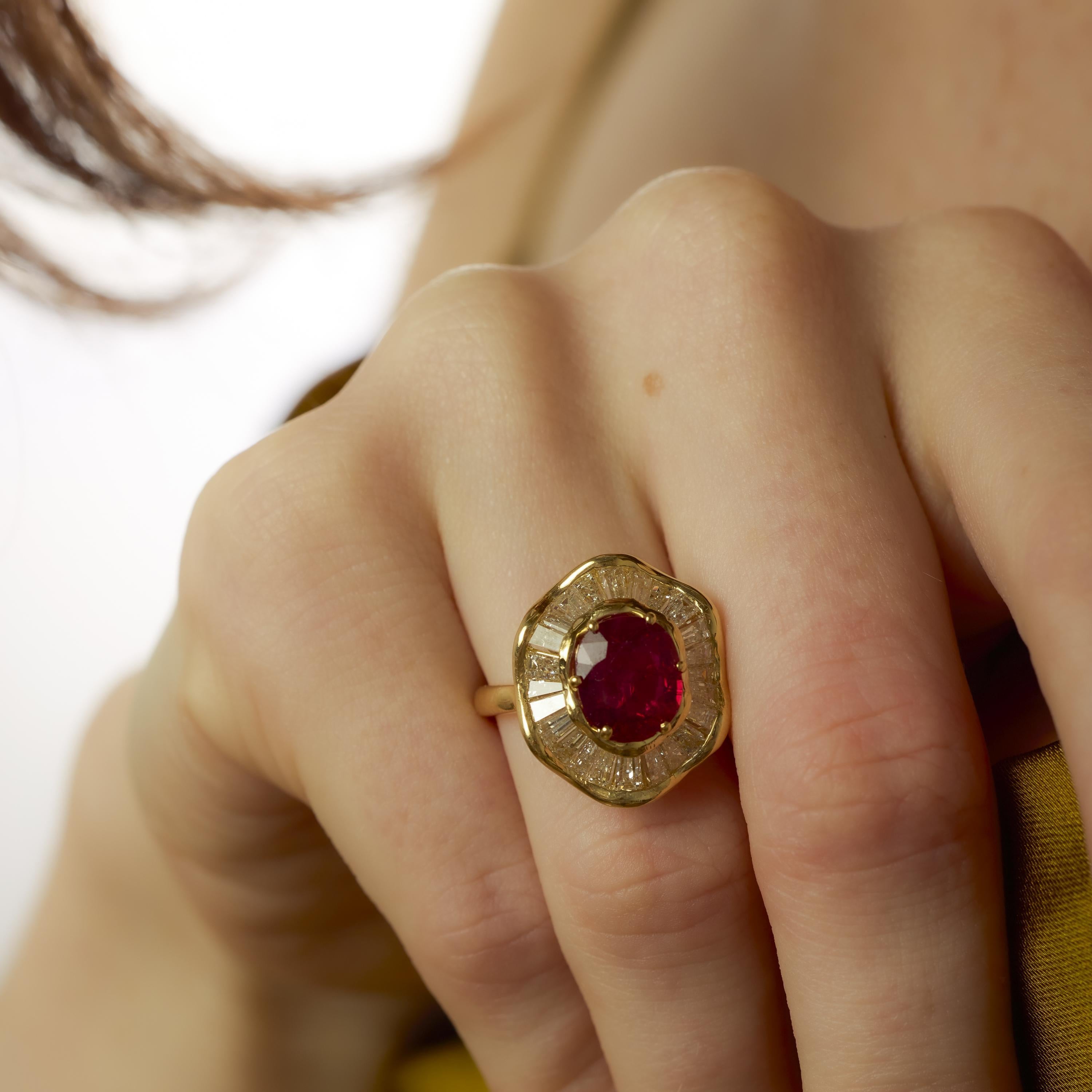 Este anillo vintage de los años 80 exhibe un vibrante rubí de corte ovalado de 2,14 quilates, certificado por el GIA (#6237593094) y tratado térmicamente para realzar su rico color. Procedente de Tailandia, el rubí está rodeado por veintitrés