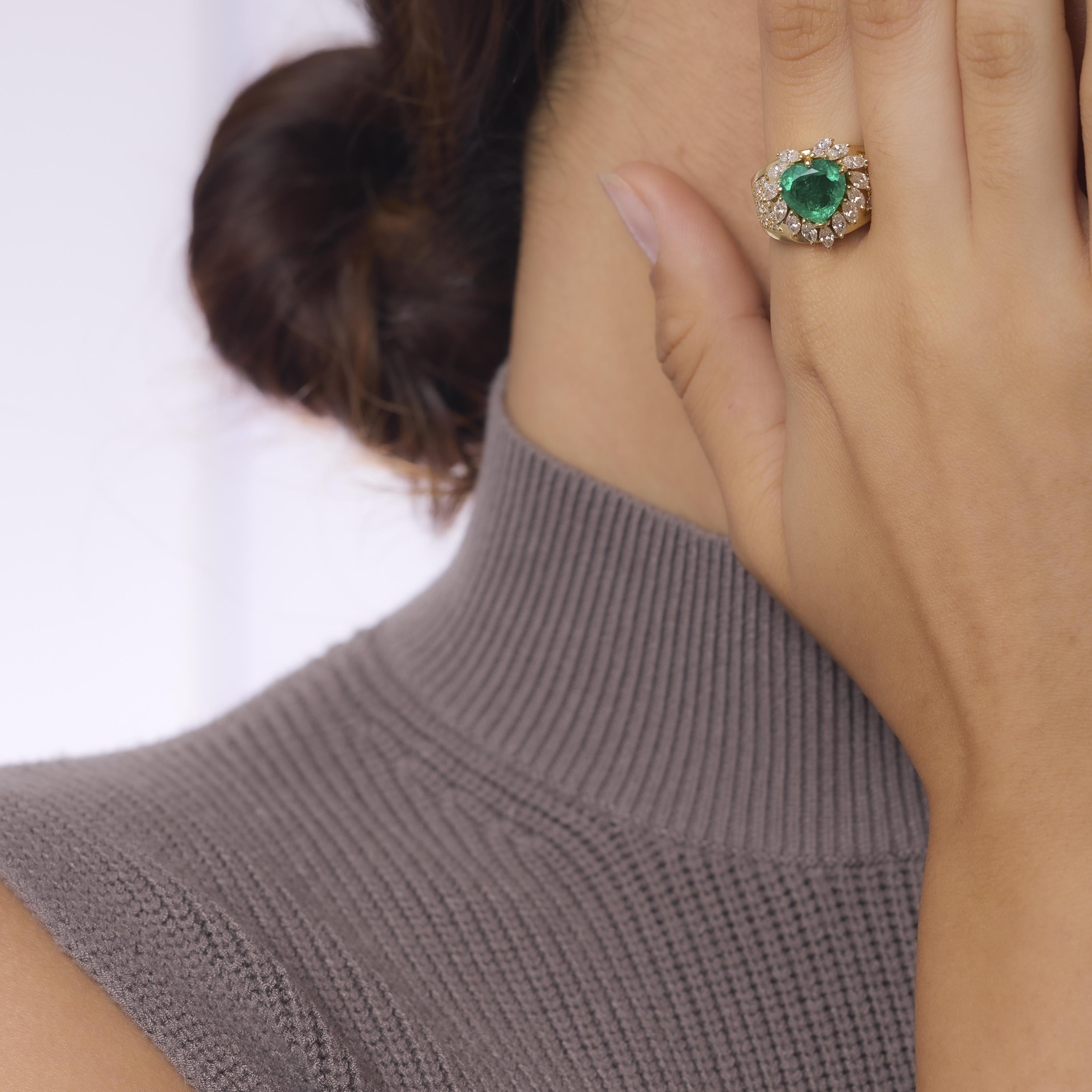 This vintage 18k yellow gold cocktail ring showcases a vibrant 2.63 carat GIA-certified heart shape emerald surrounded by 38 dazzling marquise and round brilliant cut diamonds. Crafted in the 1980s with crisp D-E color stones, the bold, romantic