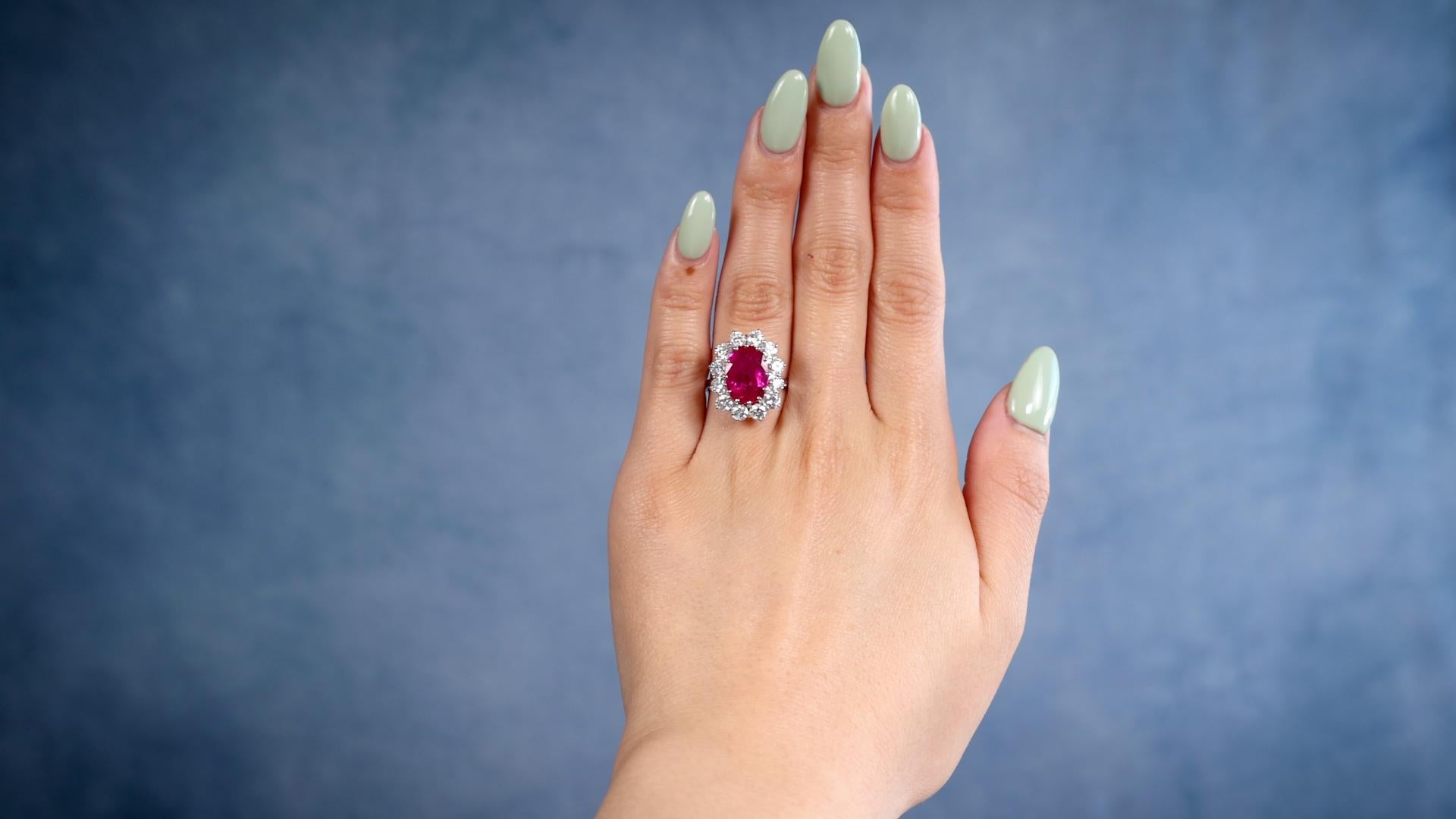 One Vintage GIA 4.26 Carat Ruby Diamond 18k White Gold Cluster Ring. Featuring one oval mixed cut ruby of 4.26 carats, accompanied by GIA #2235202950. Accented by 12 round brilliant cut diamonds with a total weight of approximately 1.85 carats,