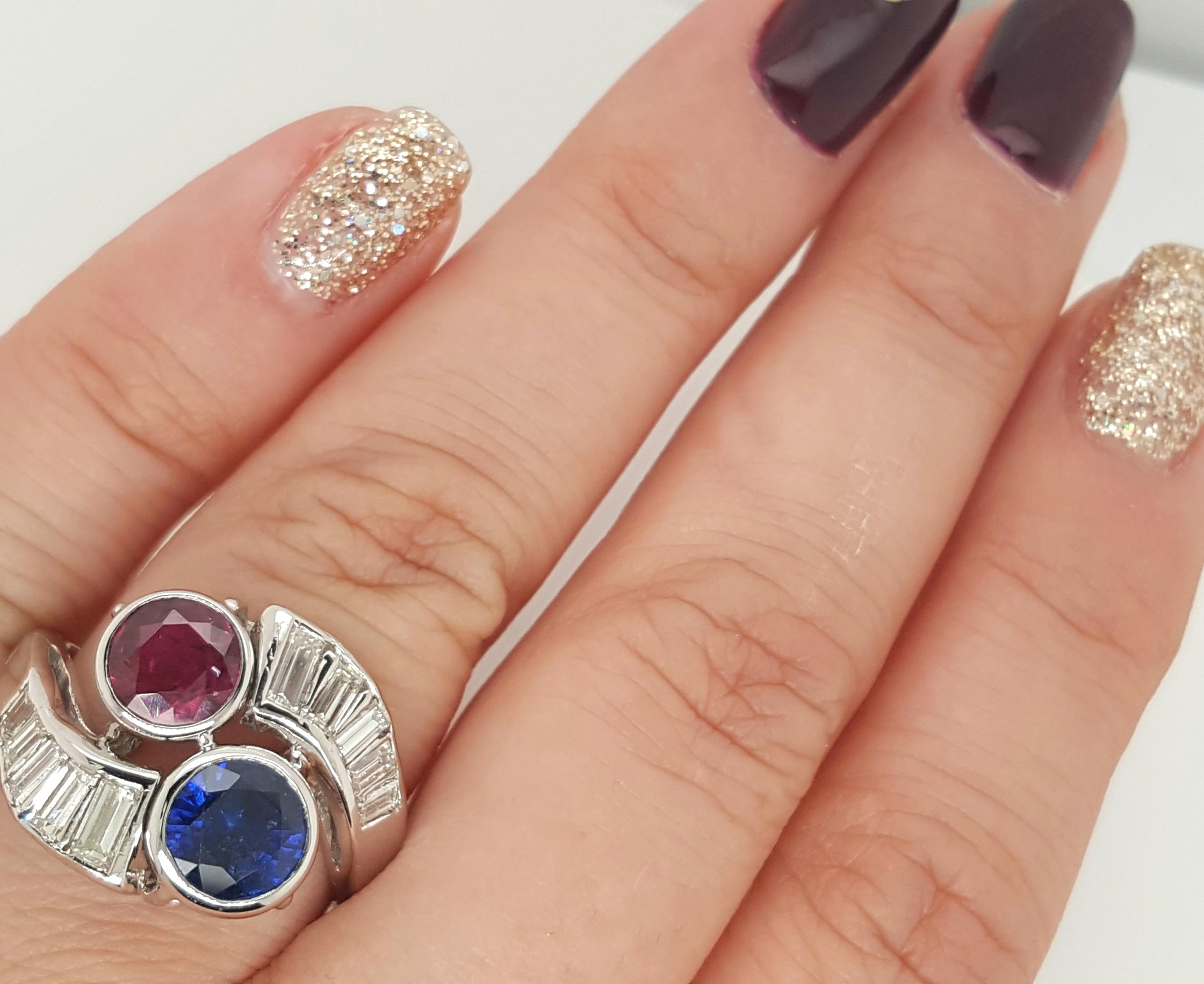 A true one of a kind Sapphire and Ruby Vintage Diamond Ring. The sapphire and ruby centers stones are bezel set and geometrically set diagonally from each other. The two stones are accented with a swirl design of baguette diamonds completing the