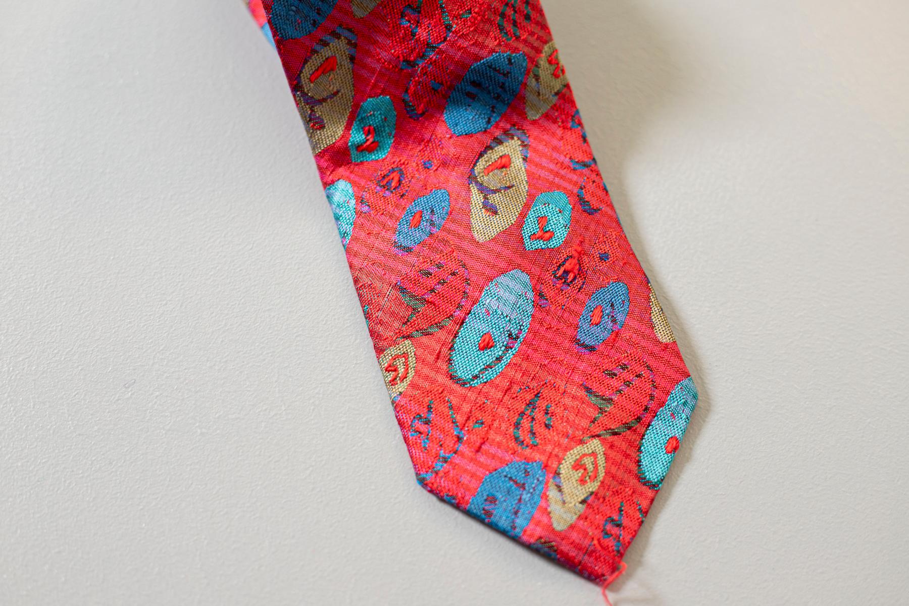 Particular and bizarre, this tie is designed by famous Italian fashion designer Gianni Versace. It is made of silk, which is why it is soft and of quality. Decorated with a bright red and with blue and light blue geometric shapes. Perfect for lovers