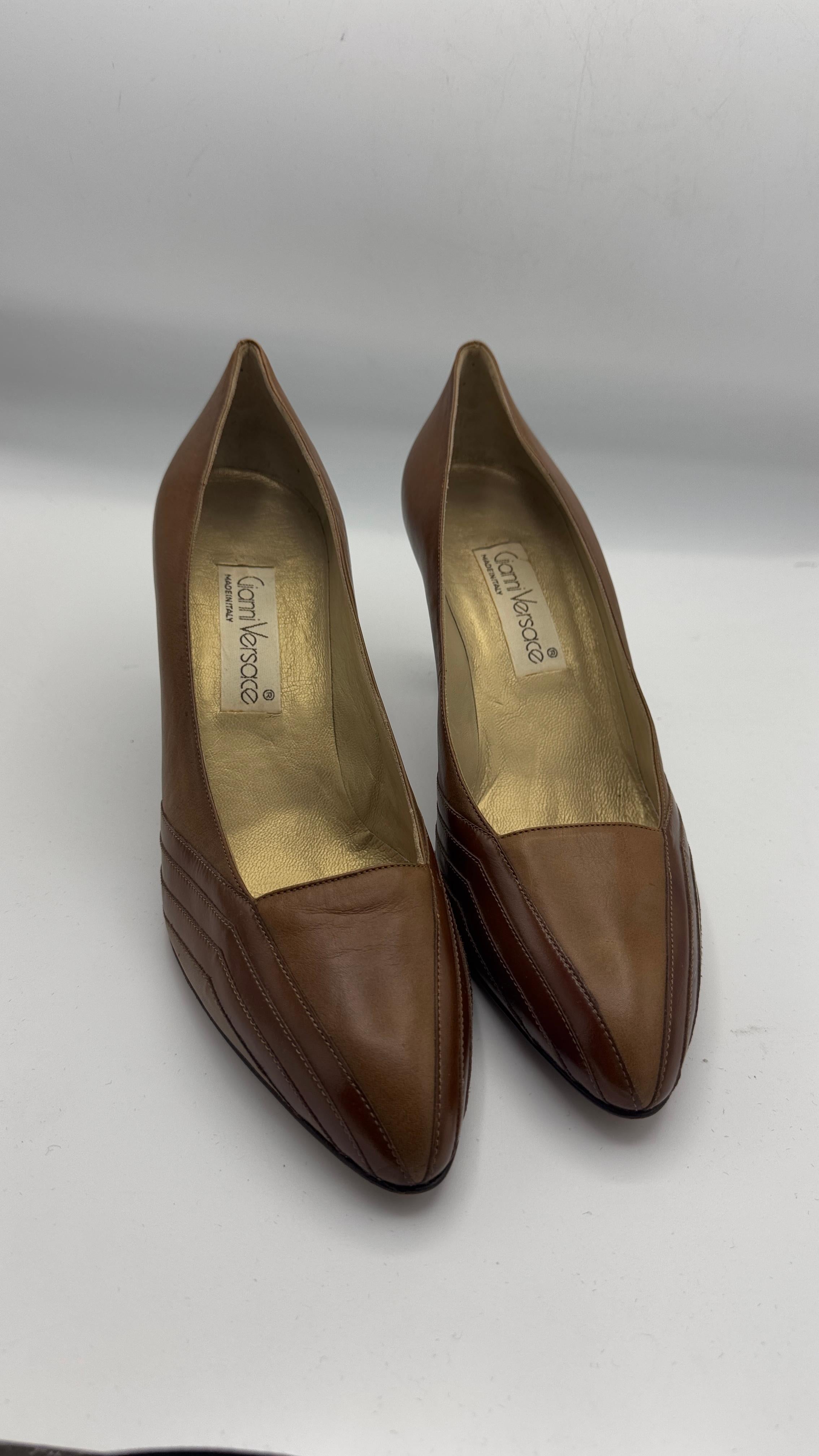 Elegantes y atemporales zapatos de salón Gianni Versace vintage confeccionados en suave piel marrón, con sutiles detalles cosidos en los laterales y una llamativa puntera en punta. El interior de piel dorada añade un toque refinado, indicativo de la