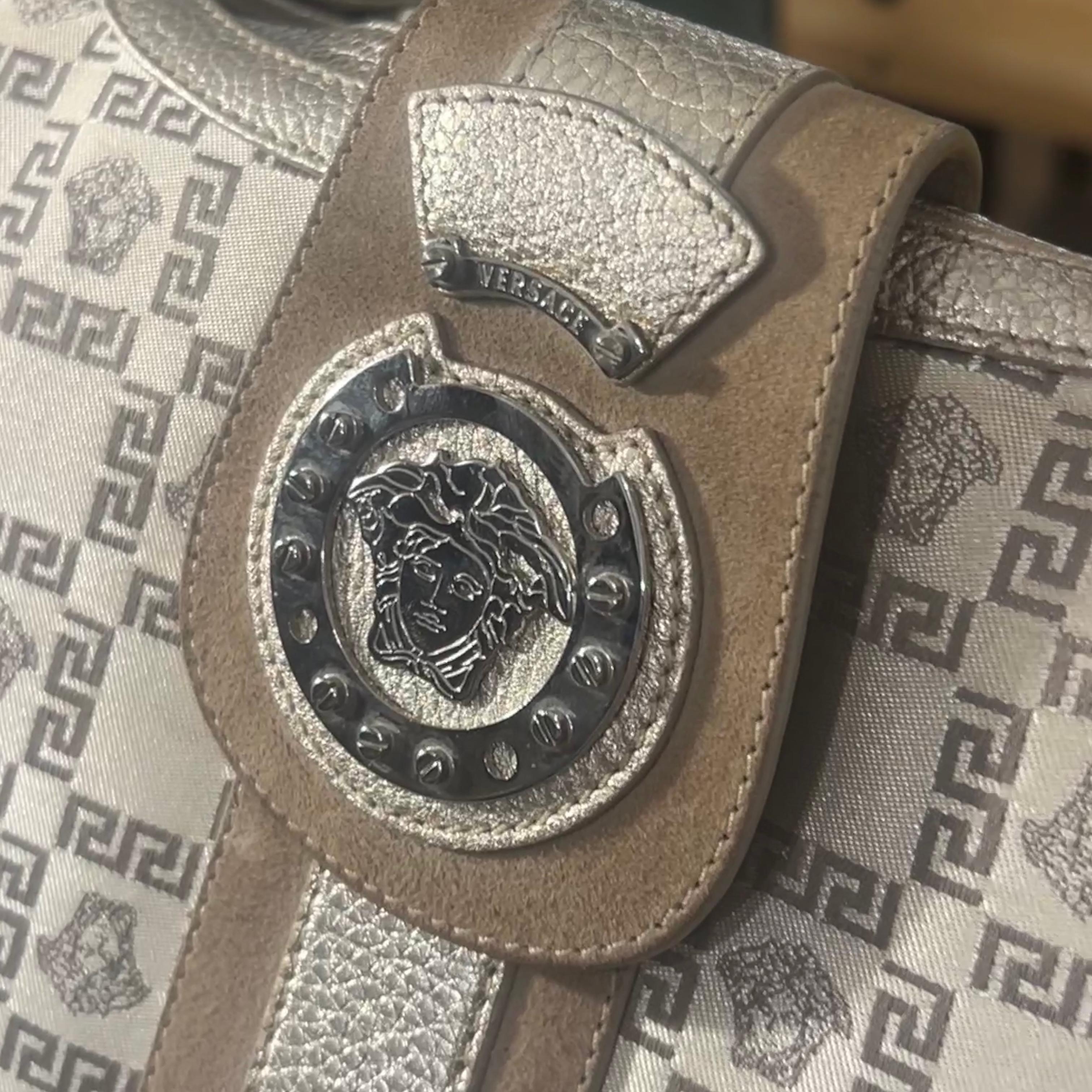 This is an exquisite vintage Versace shoulder bag, showcasing the brand's iconic aesthetic with luxurious detailing and craftsmanship. The bag features a metallic-toned leather and canvas body, adorned with a striking Greca key pattern that repeats
