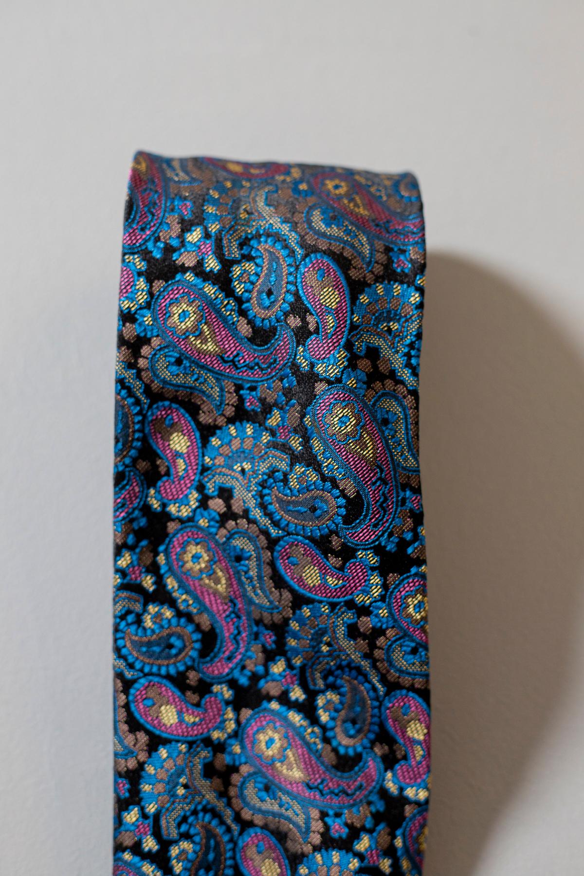 Une cravate au caractère inimitable, conçue par le célèbre designer italien Gianni Versace. Il est fabriqué en soie, c'est pourquoi il est doux et de qualité. Une cravate intemporelle, décorée de motifs paisley dans des tons de bleu et de violet.