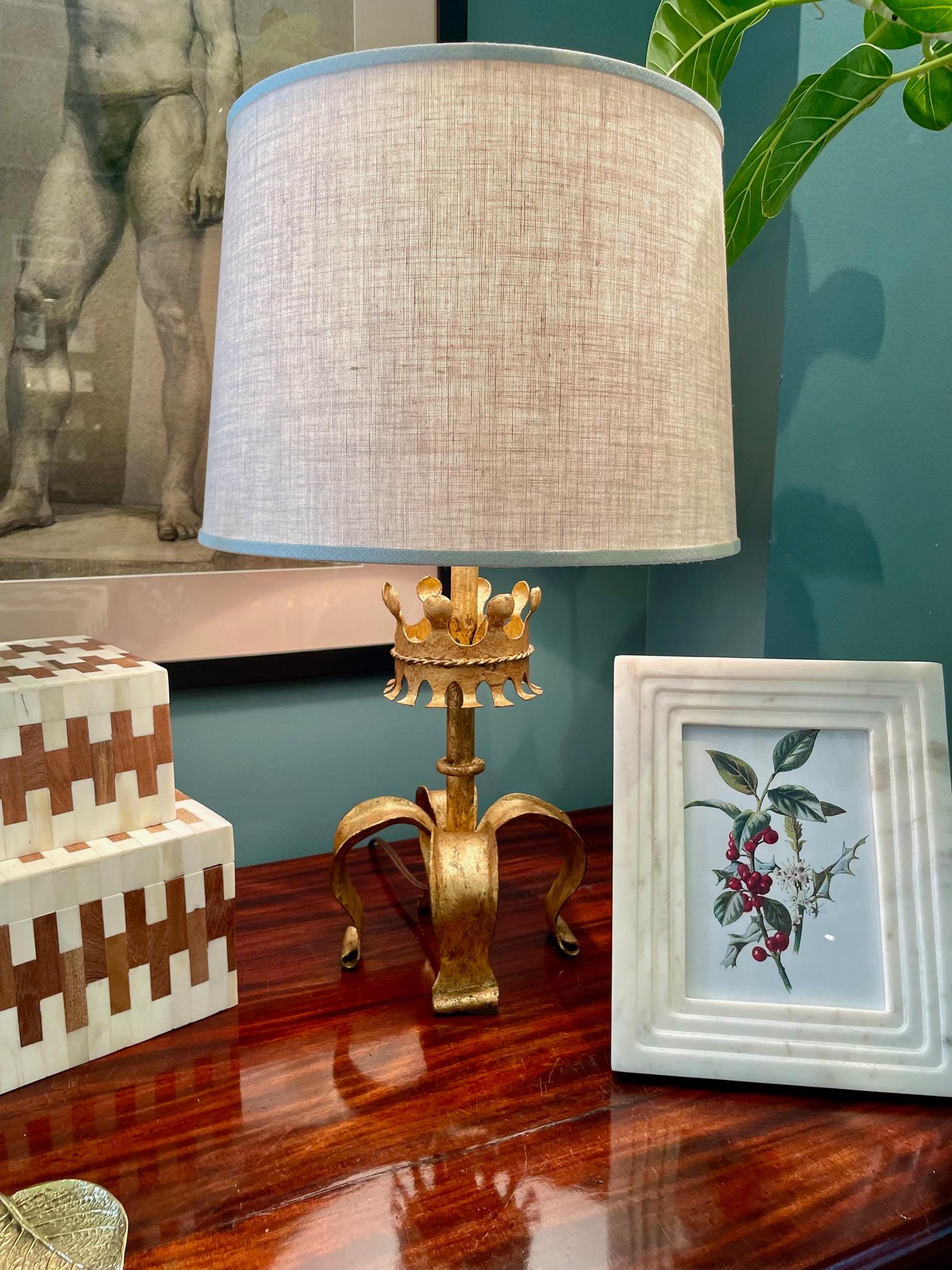 Illuminez n'importe quelle pièce avec cette élégante lampe vintage dorée au motif de couronne stylisée. Elle possède 4 pieds, une couronne décorative au centre, une finition riche en feuilles d'or, un nouvel abat-jour en lin personnalisé et a été