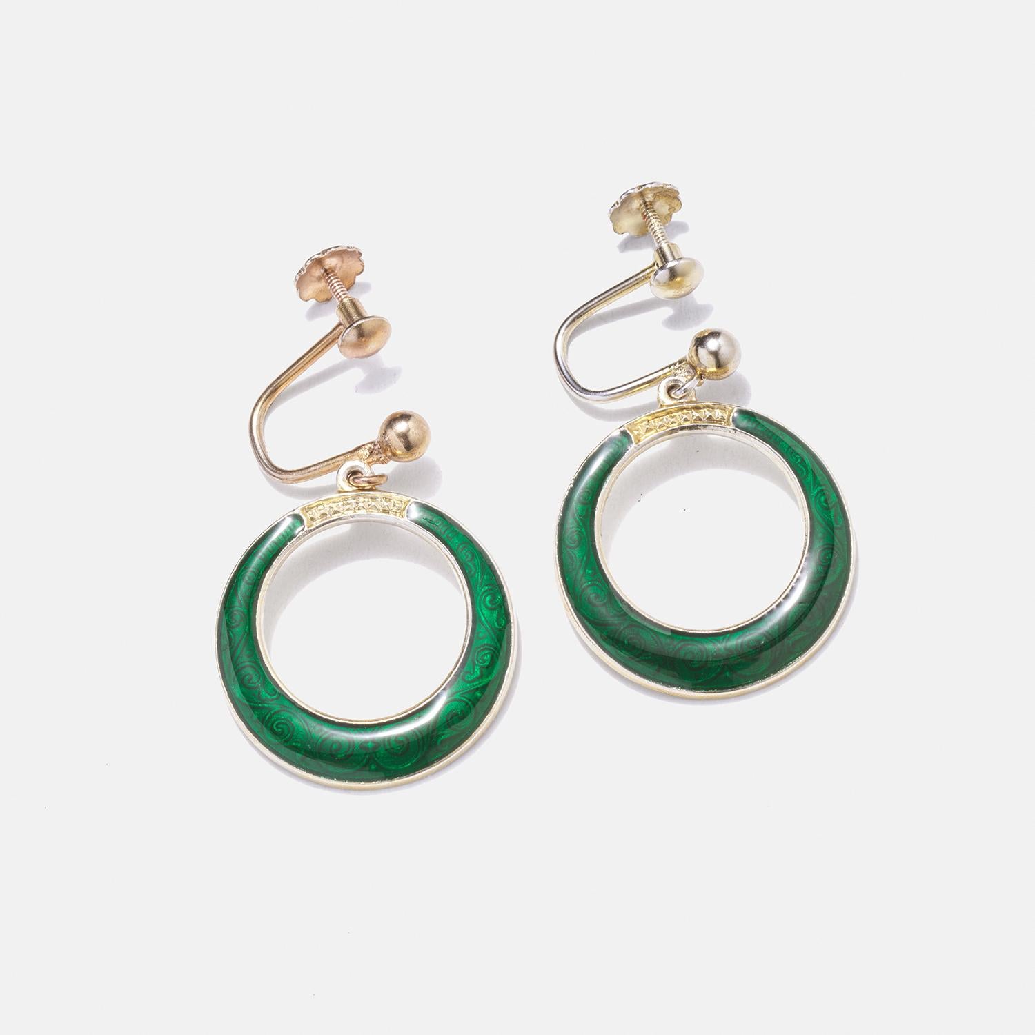 These gilded silver earrings are elegantly crafted with a round shape, featuring a vibrant green enamel inlay with an intricate filigree pattern that adds a touch of mystery. The gilded silver part of the earrings is delicately adorned with a