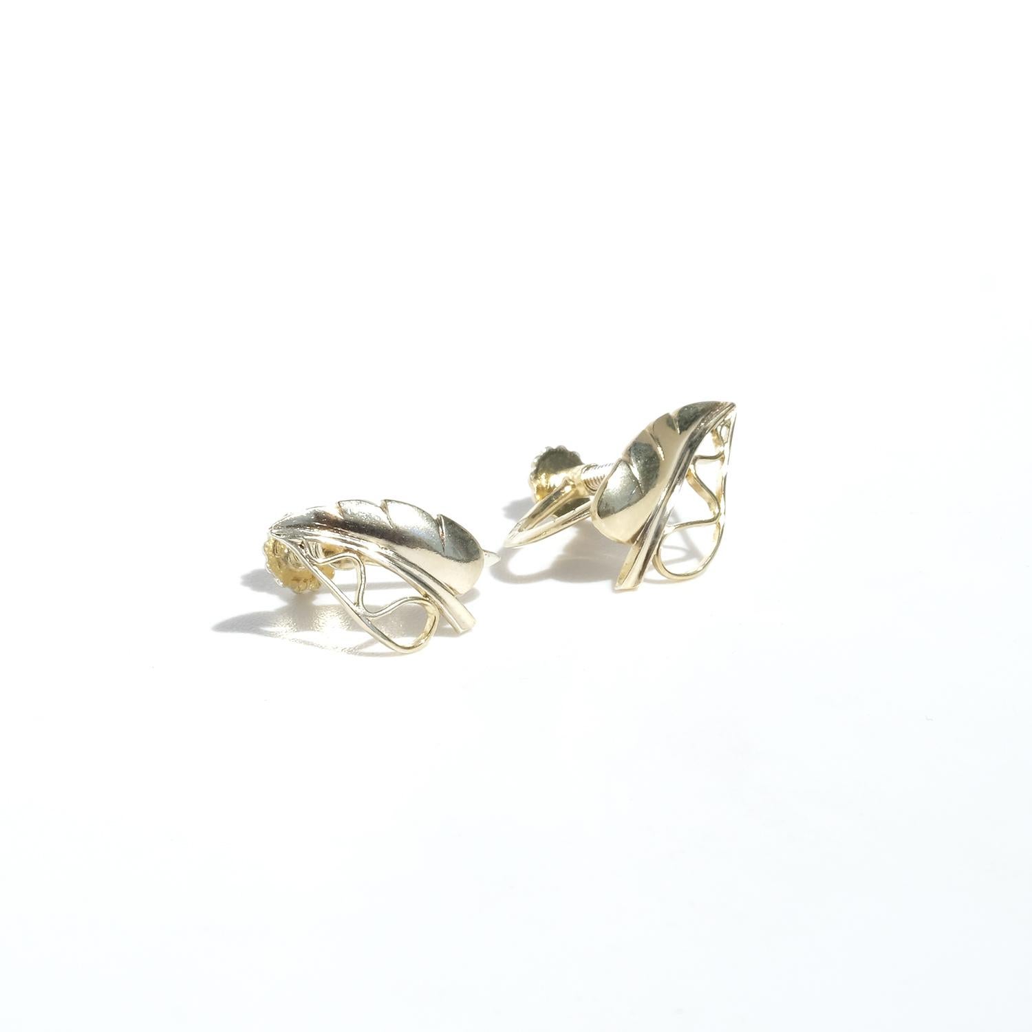 These gilded silver earrings are delicately shaped like small leaves. The leaves are detailed with fine lines and openwork, creating a realistic and intricate design. They sit beautifully on the earlobe, highlighting their elegant form. The earrings