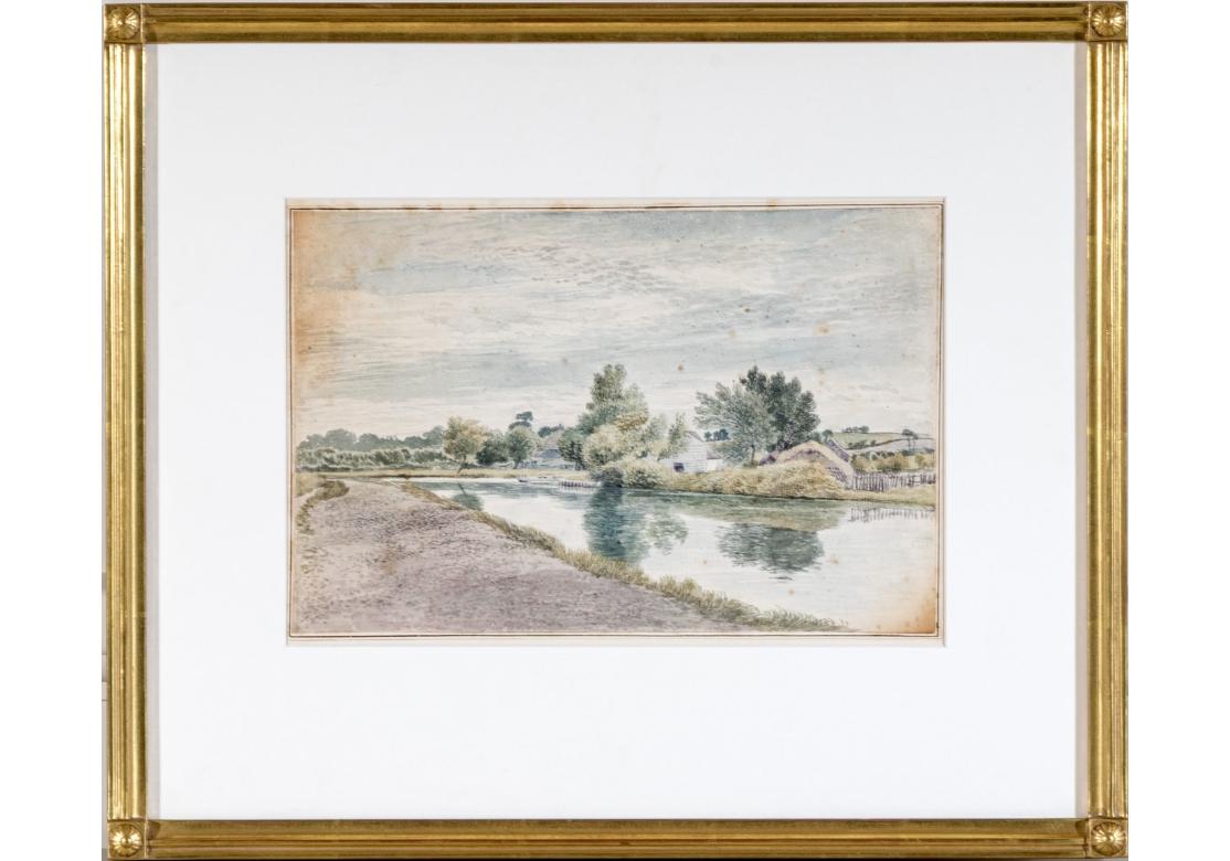 Eine zart getönte Flusslandschaft mit Häusern am von Bäumen gesäumten Ufer eines Flusses unter grauem Himmel. 
Das Aquarell ist professionell gerahmt und in einem kannelierten, vergoldeten Holzrahmen mit Eckrosetten, breitem weißem Passepartout und