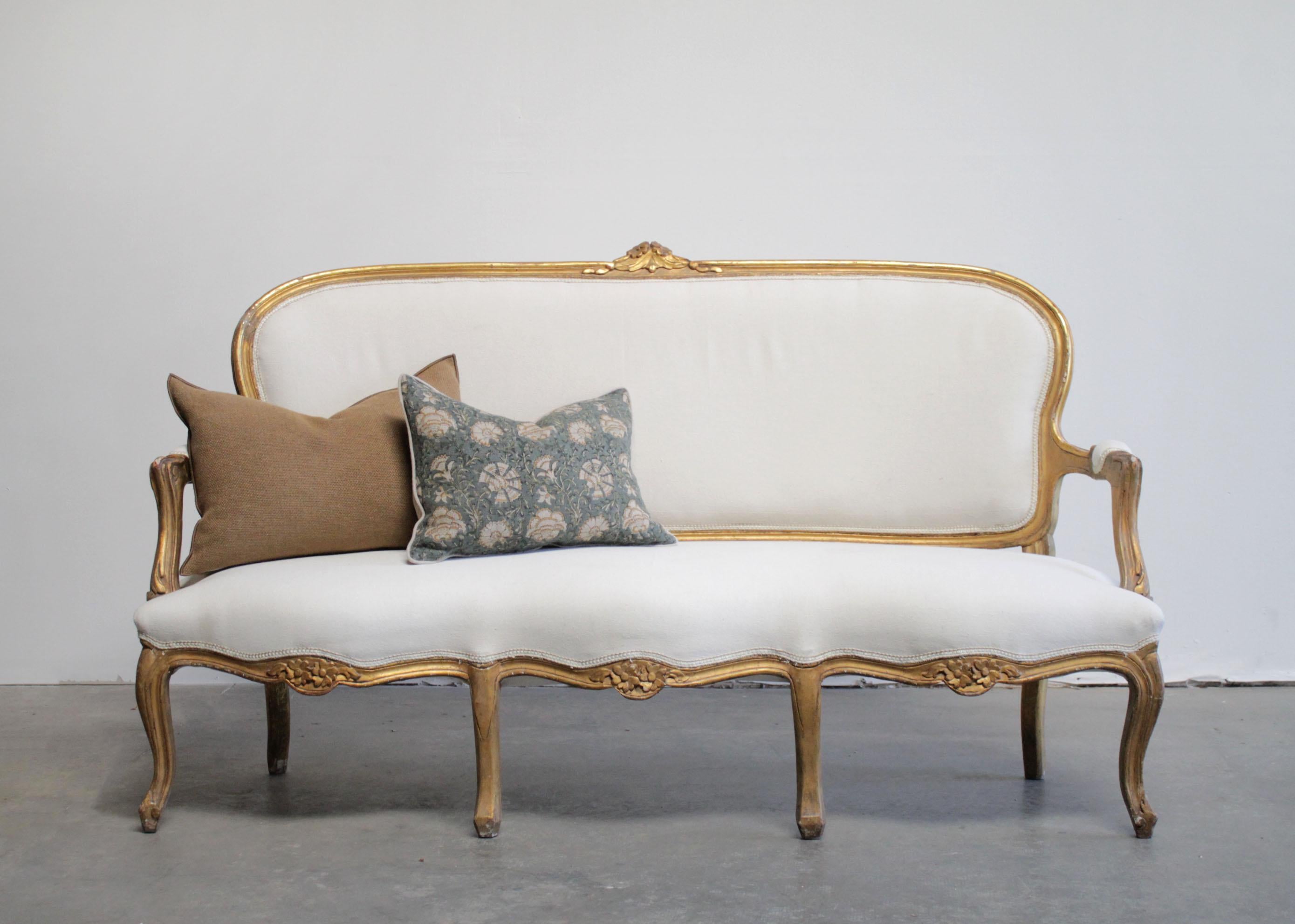 Vintage giltwood upholstered Louis XV style open arm sofa settee
Original gilt wood finish with subtle distressed edges, where gilt and wood show through.
Classic cabriole legs, with a floral carvings at the top.
Upholstered in a natural muslin