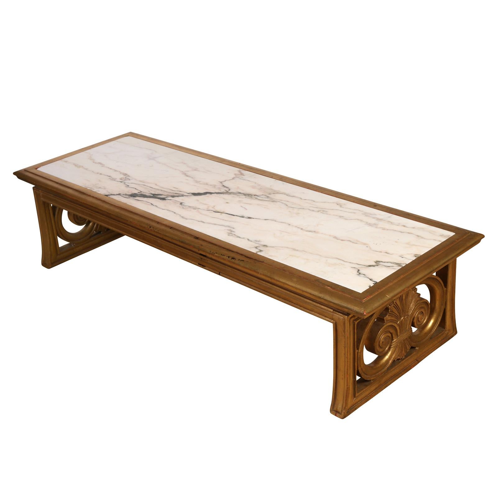 Vieille table basse rectangulaire en bois doré avec plateau en marbre blanc. La base en bois doré comprend des détails de volutes sculptées sur chaque petit côté de la table.