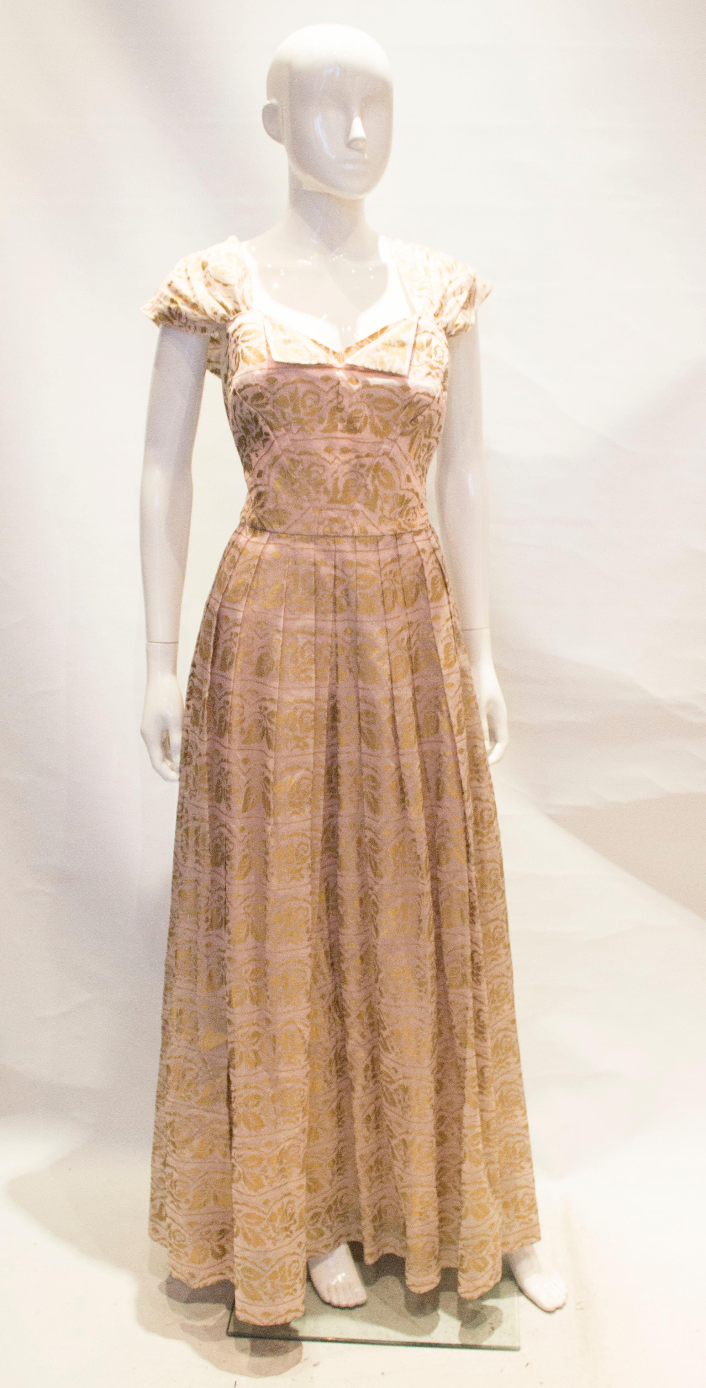 A pretty vintage party gown by Gina Couture. The dress is in a pink fabric with gold floral detail. It has a central  back zip, is fully lined and has a fold over detail at the front.