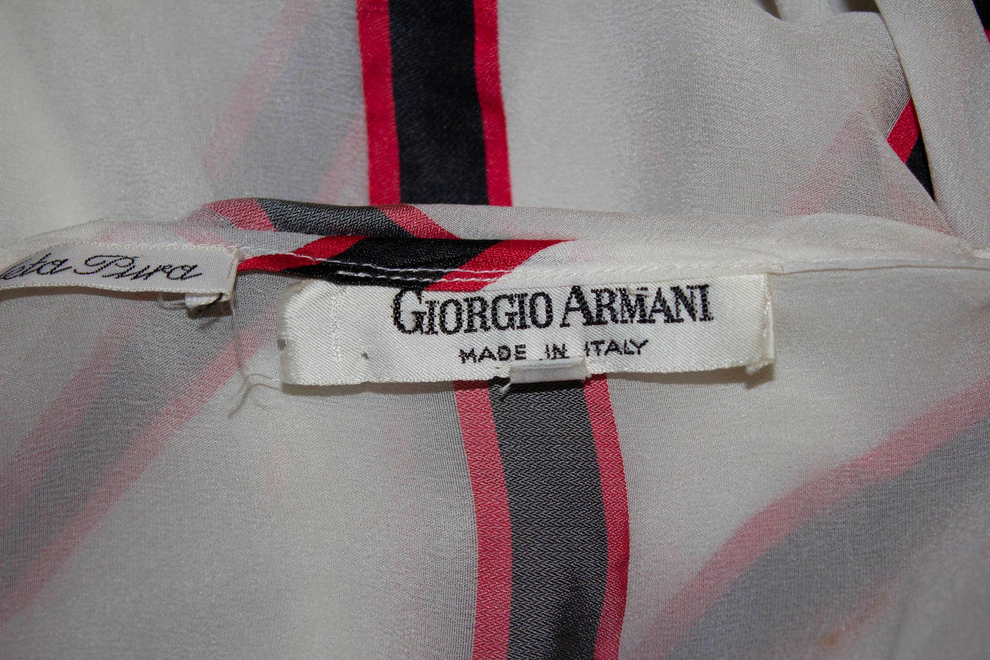 Une blouse en soie vintage chic et féminine de Giorgio Armani. Le chemisier a un fond blanc avec des détails de rayures rouges et noires. Il présente une encolure carrée, un lien au niveau du cou, deux poches sur le devant et des poignets boutonnés.