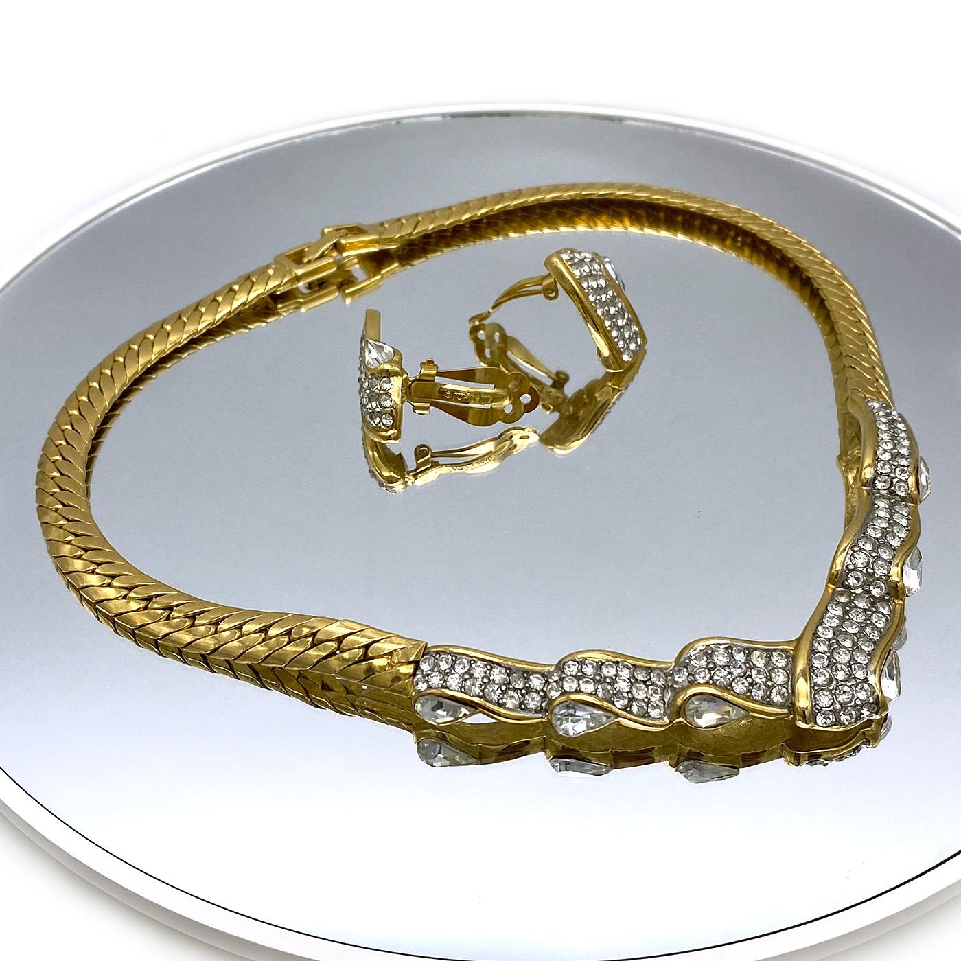 Il s'agit d'un ensemble de collier Givenchy et de boucles d'oreilles à clip. Ce collier à chevrons en or est orné de cristaux en forme de ruban. La marque Givenchy Paris/New York est inscrite sur le fermoir rabattable. Ce set classique fera