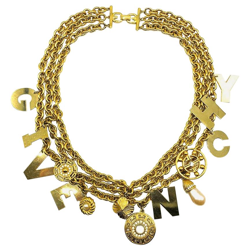 Un collare vintage con logo Givenchy. Realizzato in metallo placcato oro, cristalli e perle finte. Con tre catene di grandi dimensioni impreziosite da una serie di ciondoli incentrati sul logo, tra cui il ciondolo a forma di lettera incisa GIVENCHY