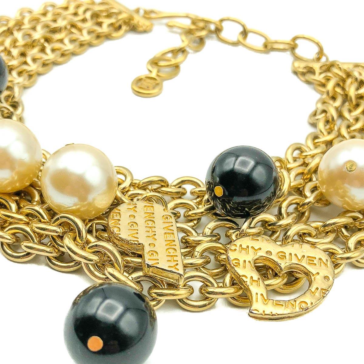 Nothing short of massive this Vintage Givenchy Chain Charm Collar is a fabulous find. Crafted in gold plated metal and resin beads. Featuring five fabulous chunky chains dropping with twelve charms including black and pearl resin beads, logo