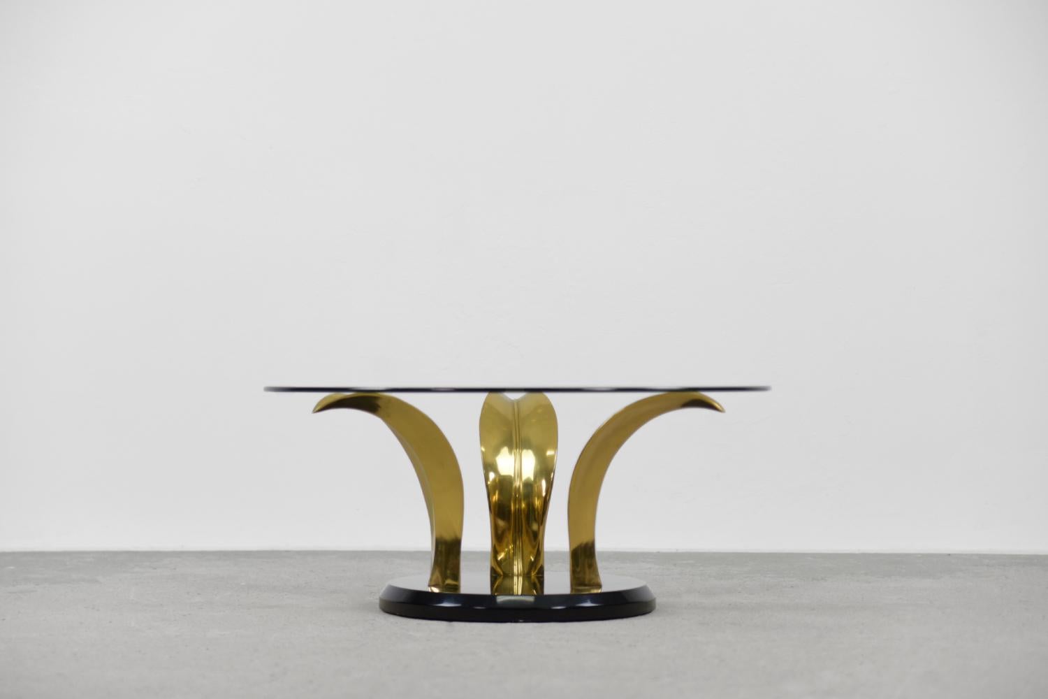 This very rare cocktail table was made in the United States during the 1970s. The striking base consists of three palm leaves made of brass and mounted on a black lacquered stone base. The round top is made of thick tempered glass. The table refers