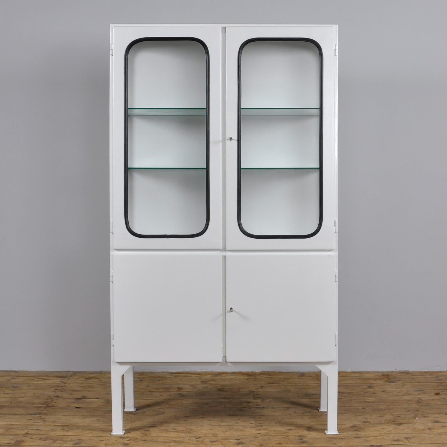 This medical cabinet was designed in the 1970s and was produced circa 1975 in Hungary. It is made from iron and glass, and the glass is held by a black rubber strip. The cabinet features two adjustable glass shelves and functioning locks. The