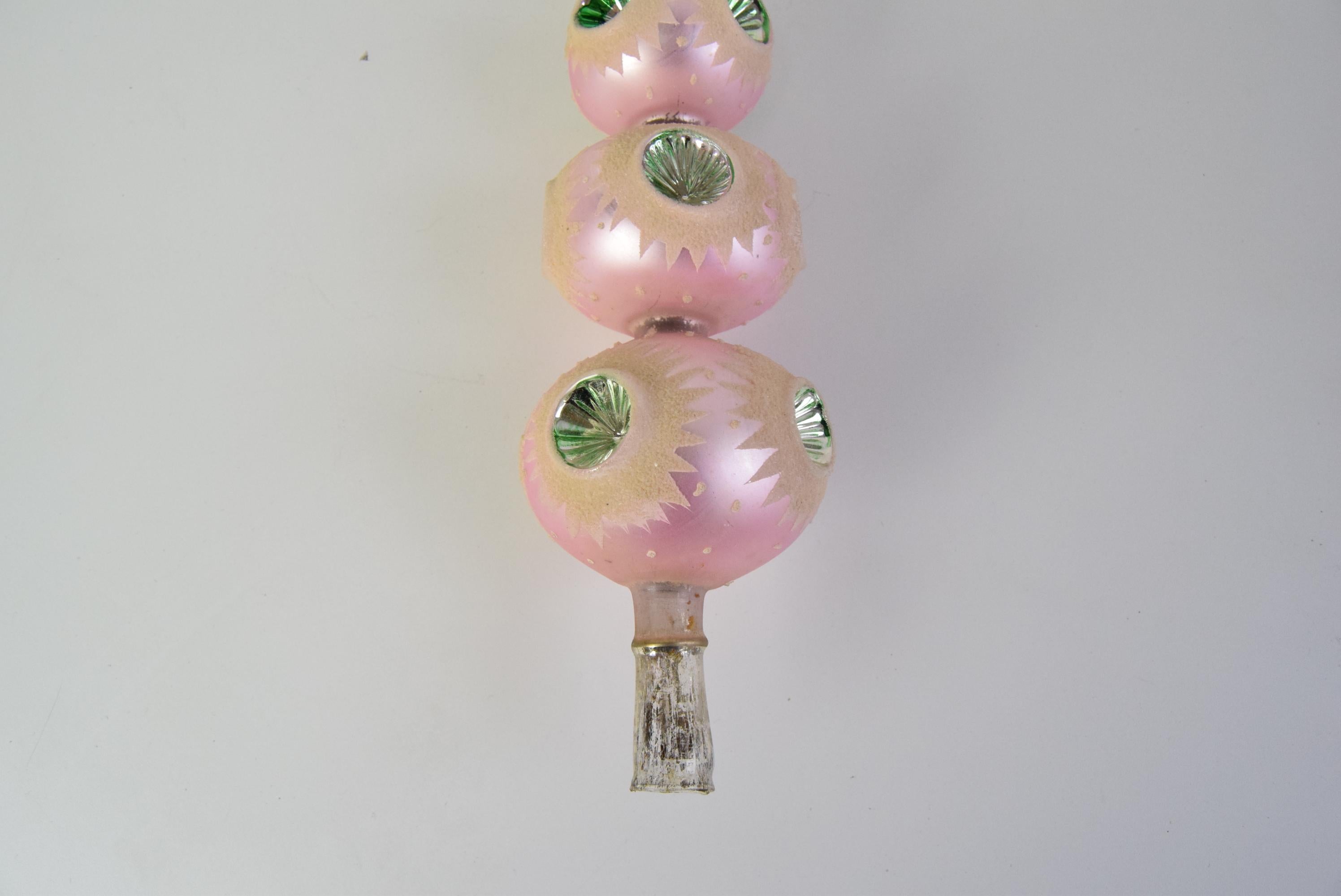 Ein wunderschönes Glasornament für den Weihnachtsbaum. Es hat eine gestufte Struktur mit einem zartrosa Farbton und kreisförmigen Einkerbungen, die mit grünen Akzenten verziert sind.
Es ist eine auffällige Ergänzung für die festliche Umgebung oder
