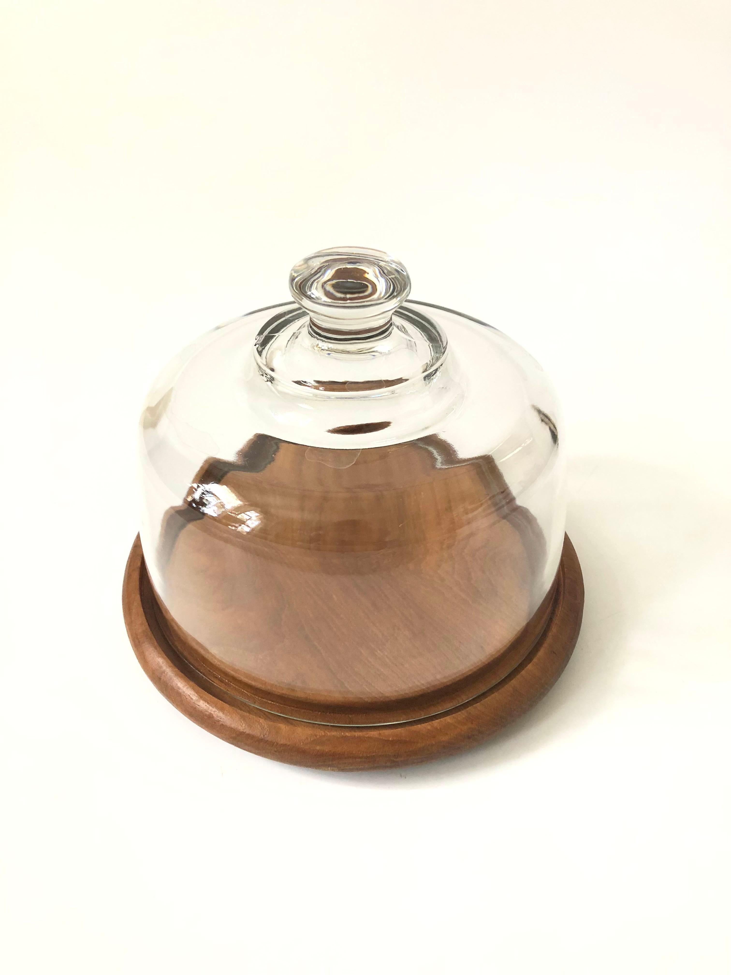 A vintage glass cloche. The top is made of heavy glass with an integrally formed handle sitting on a circular teak base. A circular groove is routed into the base to keep the glass dome in place. Perfect for serving appetizers or cheeses.