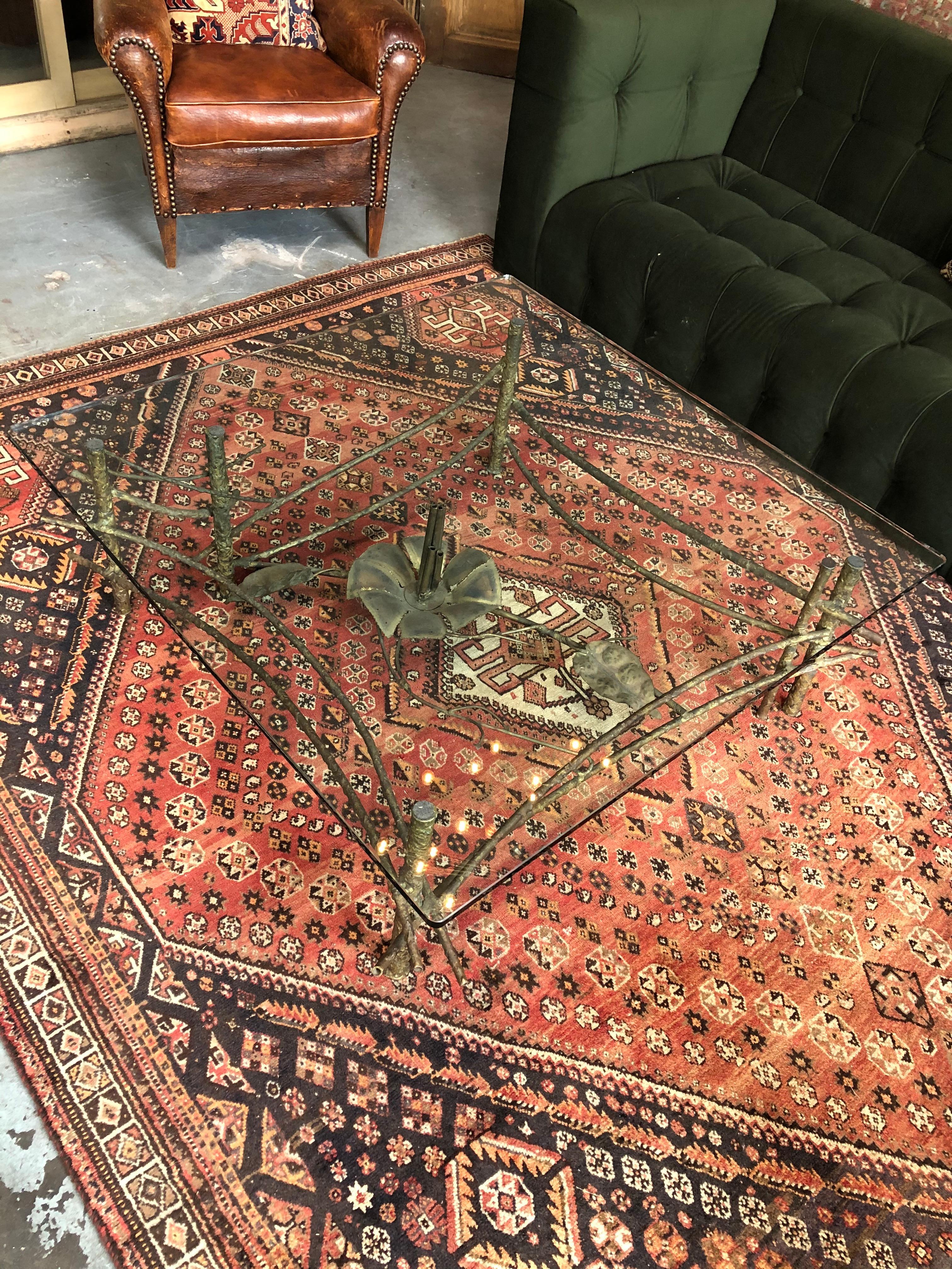 Early 1900s glass coffee table with an ornate floral iron table base. Base has a large lotus looking flower at the center. Glass evenly sits on all four corners with pads on each leg as to not scratch the tabletop.
 