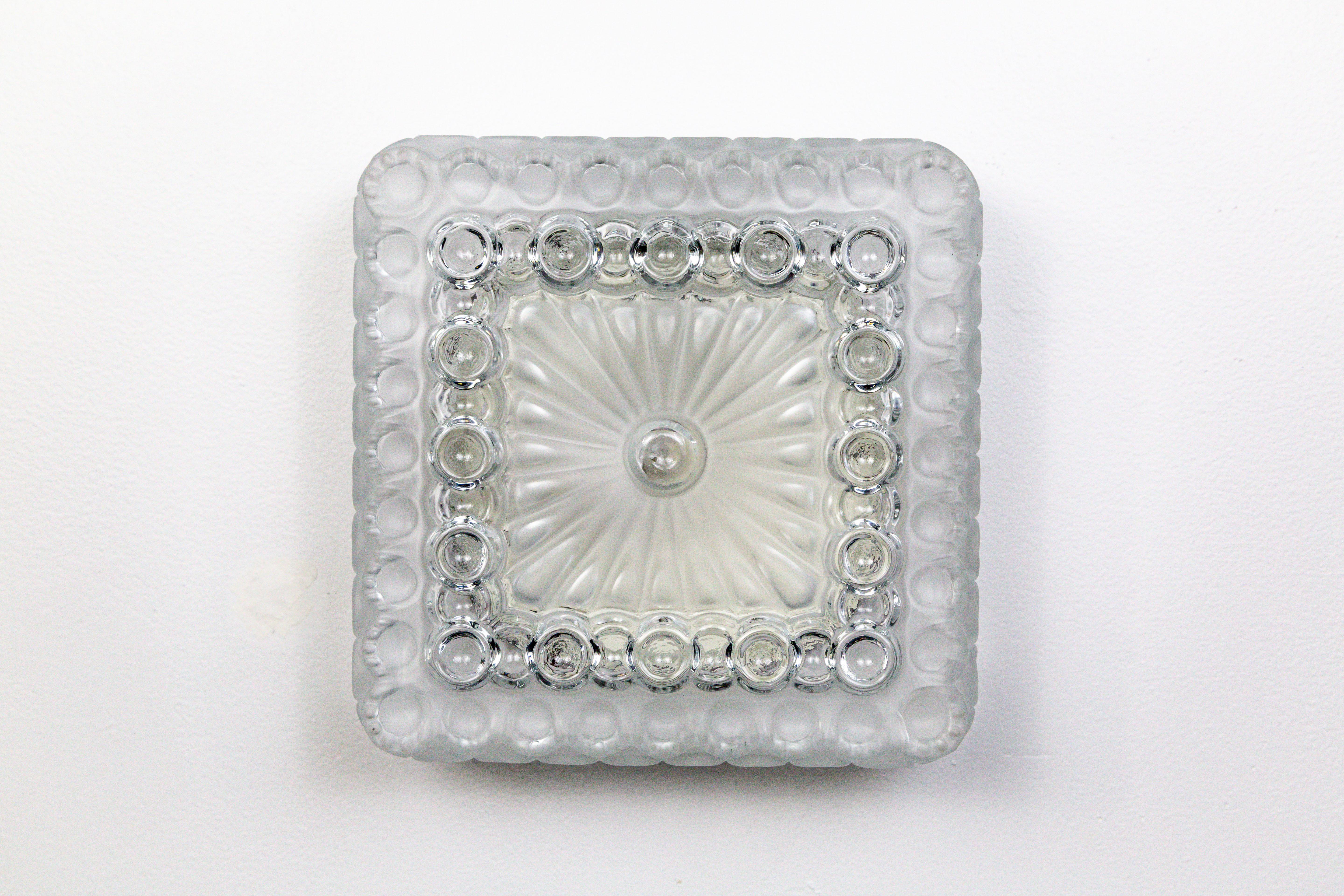 A fabulous, frosted and clear, molded glass sconce with circular designs trimming its square shape. It looks great oriented as a diamond or a square; as a wall light or on a ceiling, 1970s. A porcelain, medium base socket, and black, metal
