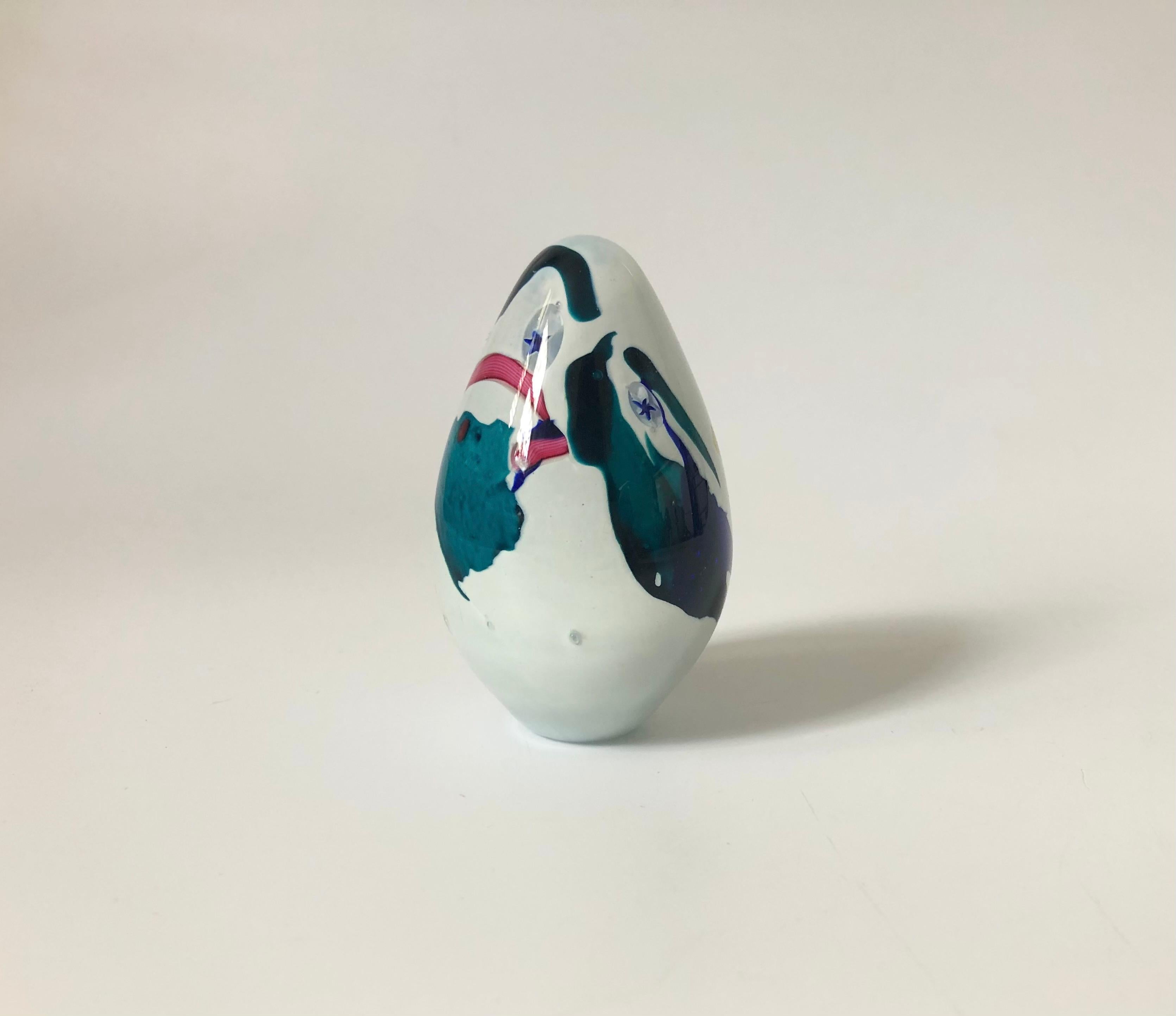 A vintage egg shaped art glass paperweight, made in 1994 by Glass Eye Studio. Opaque white color to the interior with abstract shapes of colorful glass throughout and some small stars embedded in the glass. Marked on the base 