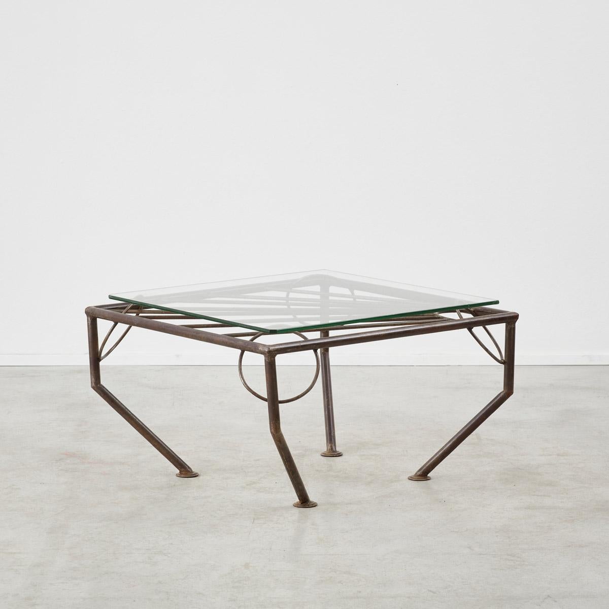 Beaming out like a sunburst, this forged metal coffee table has a dynamic shape. The glass is balanced upon four protruding rings, which despite its precarious look sits firmly in place. 

The metal base has a lovely oxidised patina. The glass top