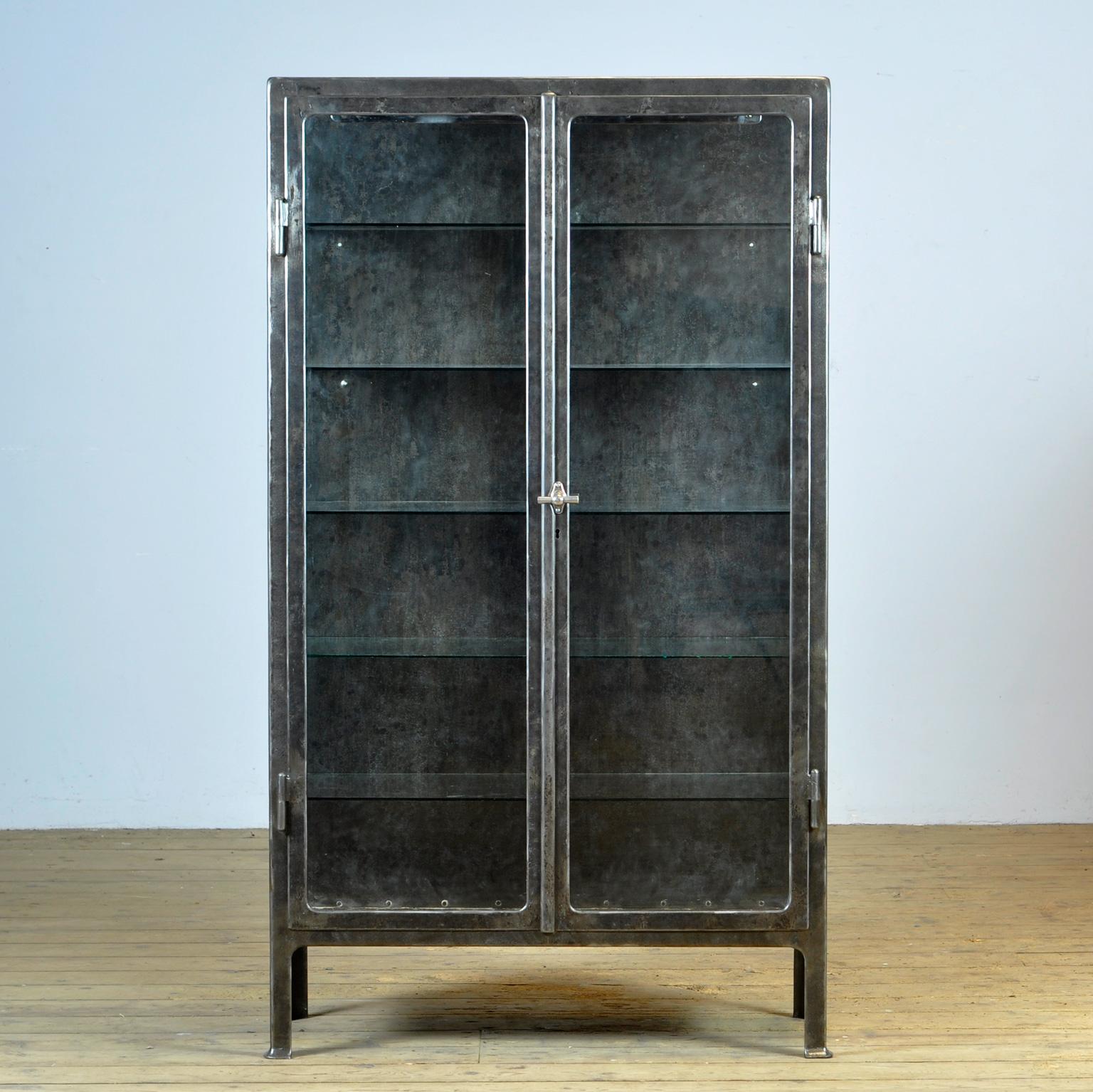 Riveted heavy iron cabinet with the original lock and handle, made around 1920. The cabinet has been stripped to the metal and treated against rust. The cabinet was probably used in a laboratory or hospital. On the inside, the cupboard has an enamel