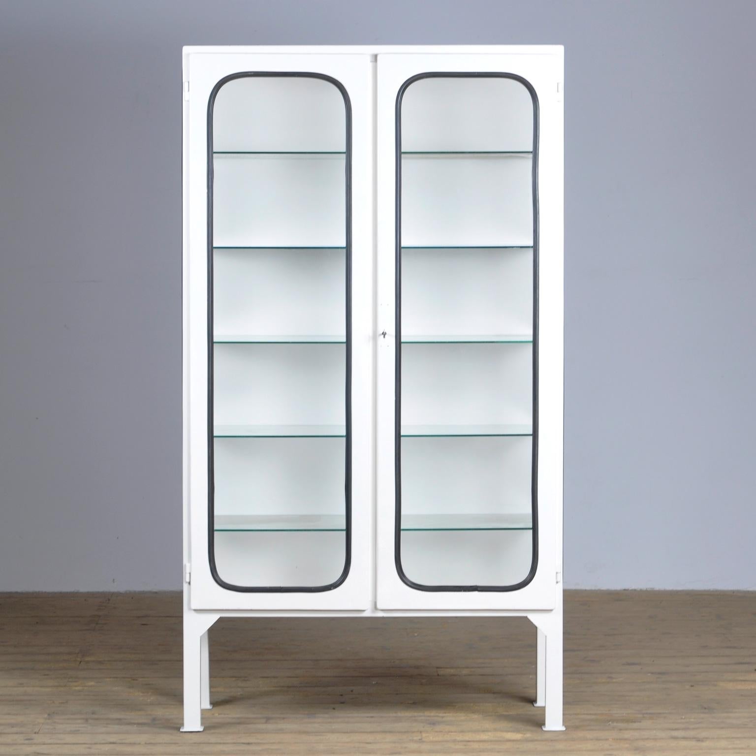 This medicine cabinet was designed in the 1970s and was produced circa 1975 in Hungary. It is made from iron and glass, and the glass is held by a black rubber strip. The cabinet features five adjustable glass shelves and a functioning lock.